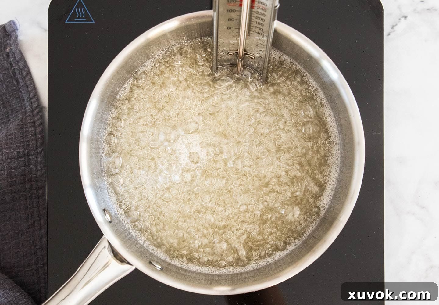 The sugar syrup bubbling vigorously in a saucepan with a candy thermometer attached, reaching optimal temperature.