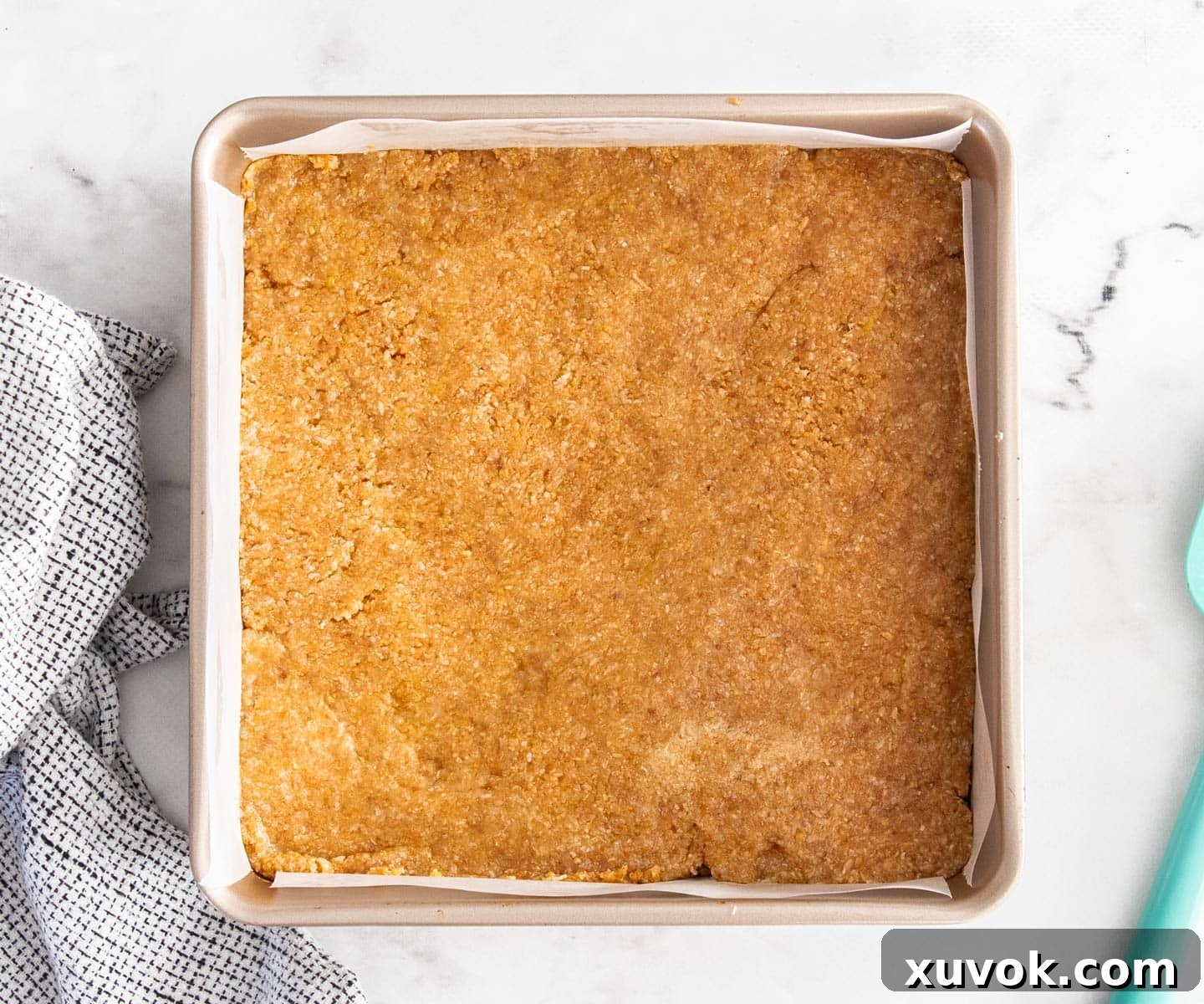 The firm biscuit base pressed evenly into a square baking pan lined with parchment paper.