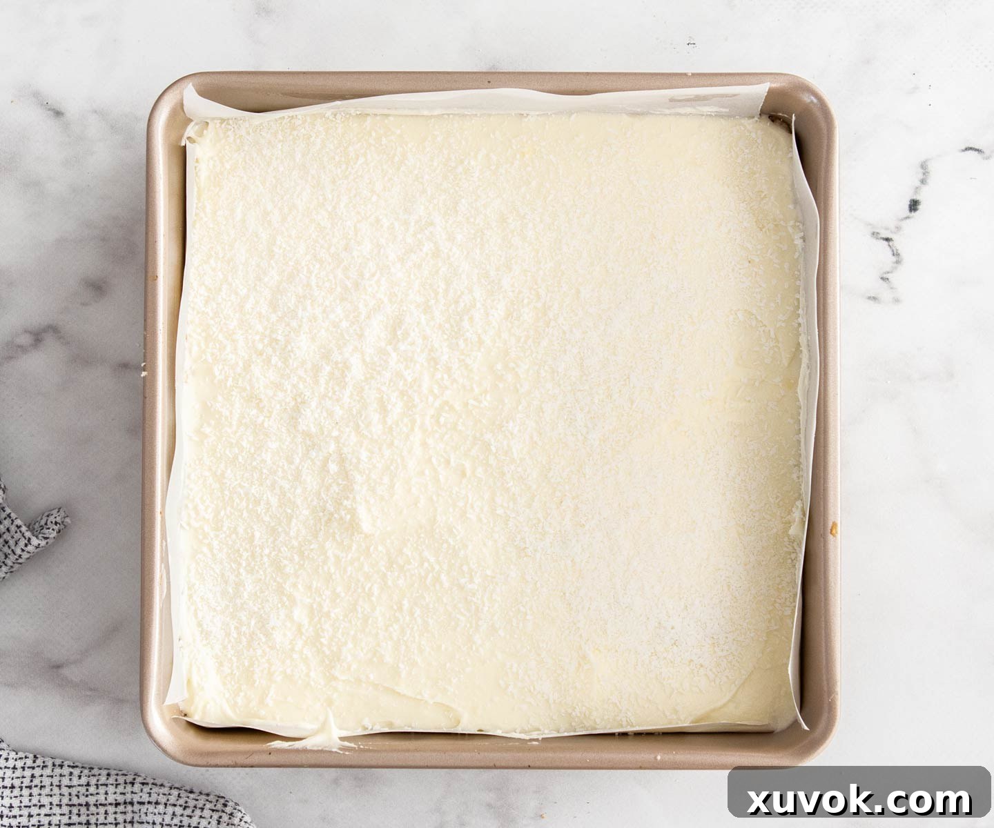 The complete coconut lemon slice, topped with a smooth layer of frosting and sprinkled with coconut, ready to be chilled.