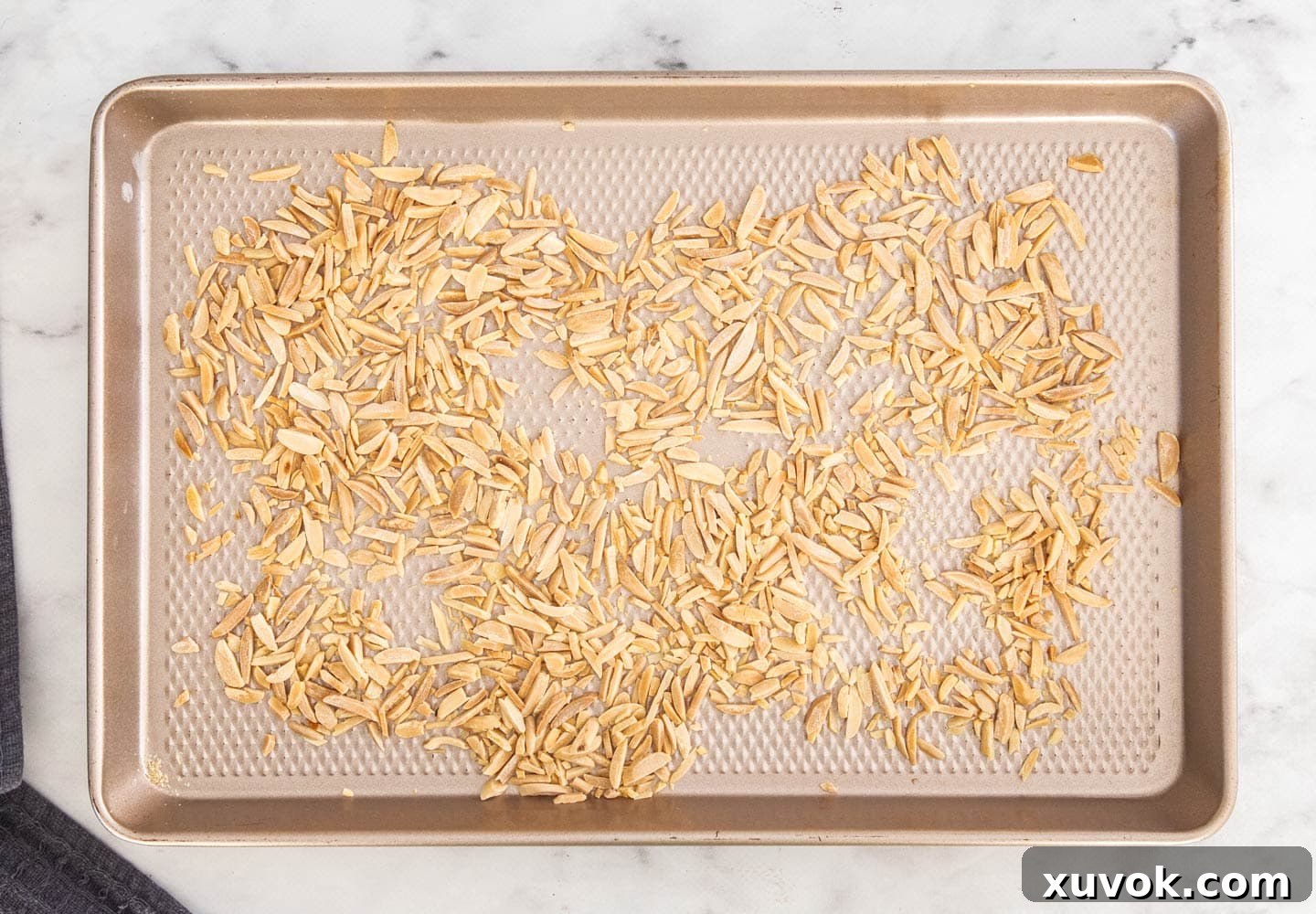 Toasted slivered almonds spread evenly on a baking sheet, showing their light golden brown color.