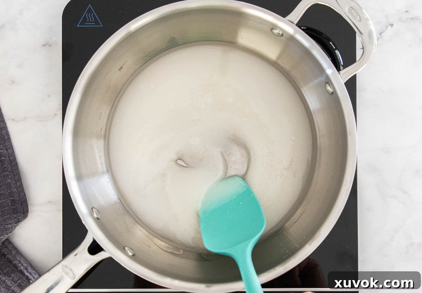 Granulated sugar dissolving into water in a stainless steel saucepan over gentle heat.