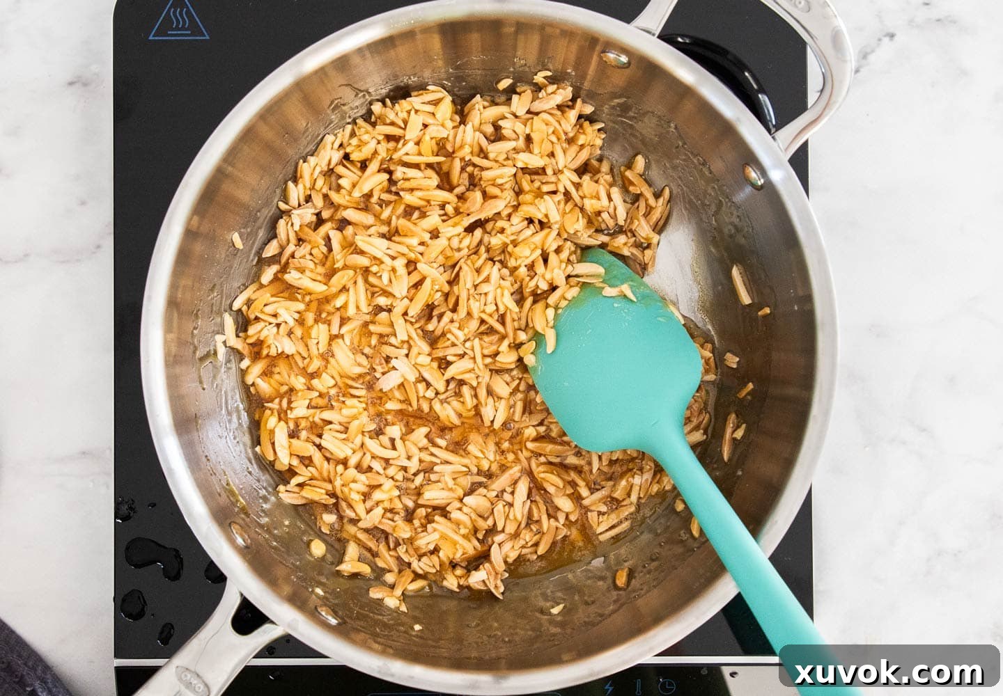 Toasted slivered almonds being stirred into the hot, golden toffee in a saucepan.