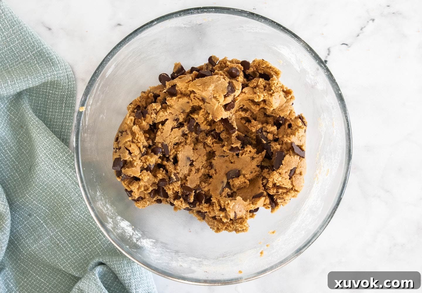 The ultimate chocolate chip cookie dough in a clear glass bowl, studded with generous amounts of dark chocolate chips and chunks.