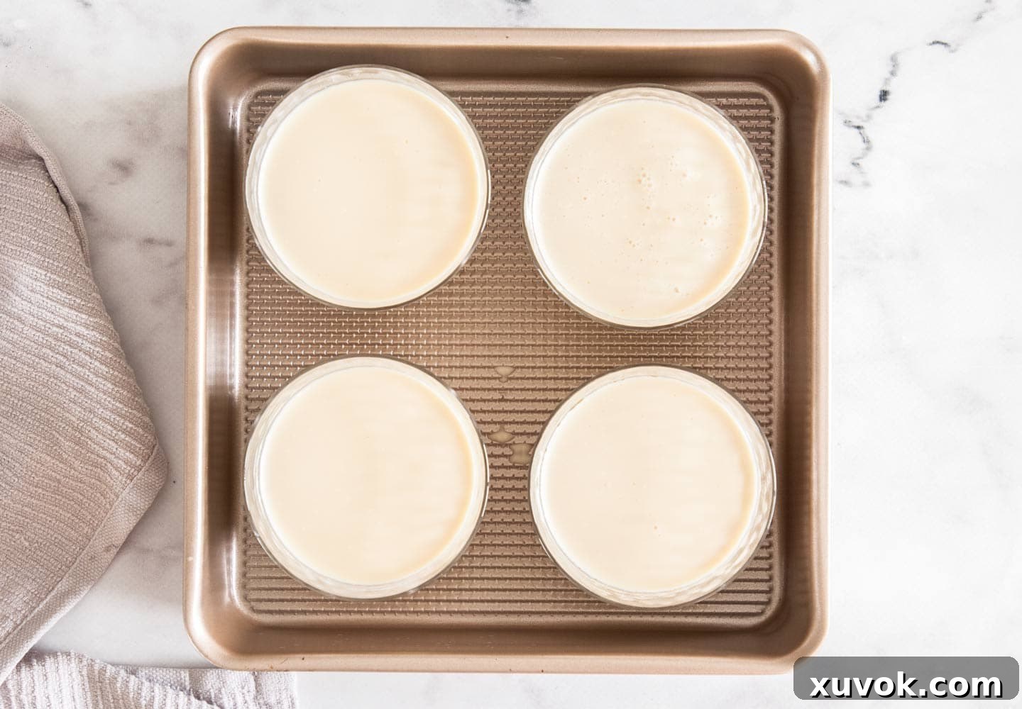 The panna cotta mixture in glasses sitting inside a square baking pan.