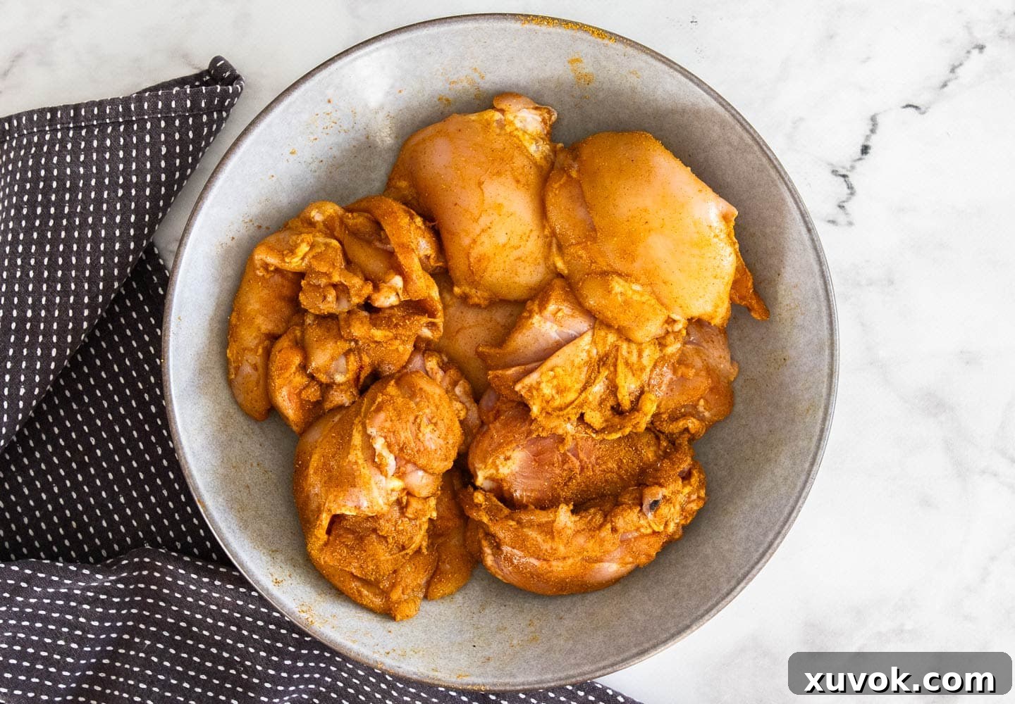 The chicken thighs in a bowl, rubbed with seasoning.