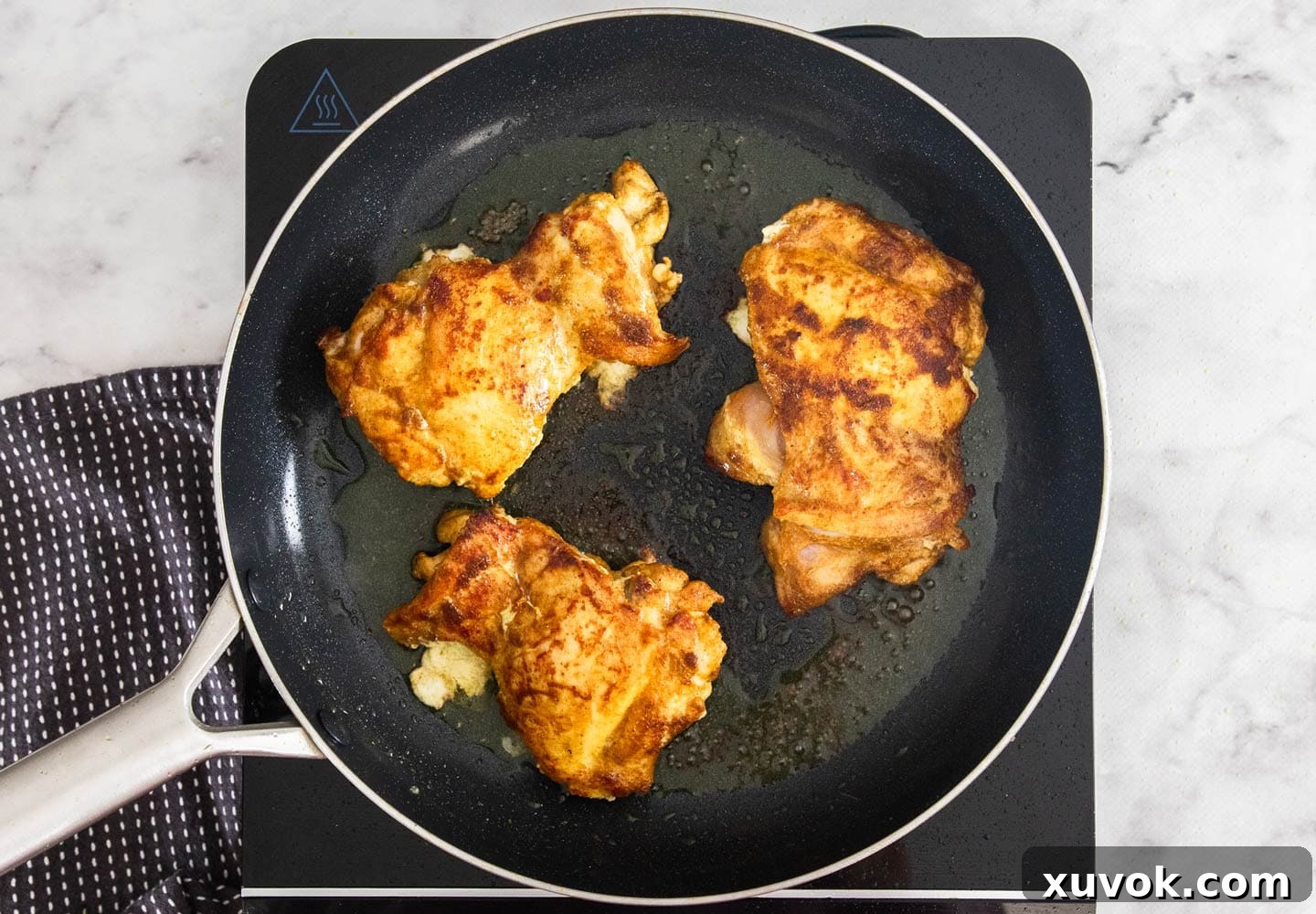 The chicken thighs searing in a pan.