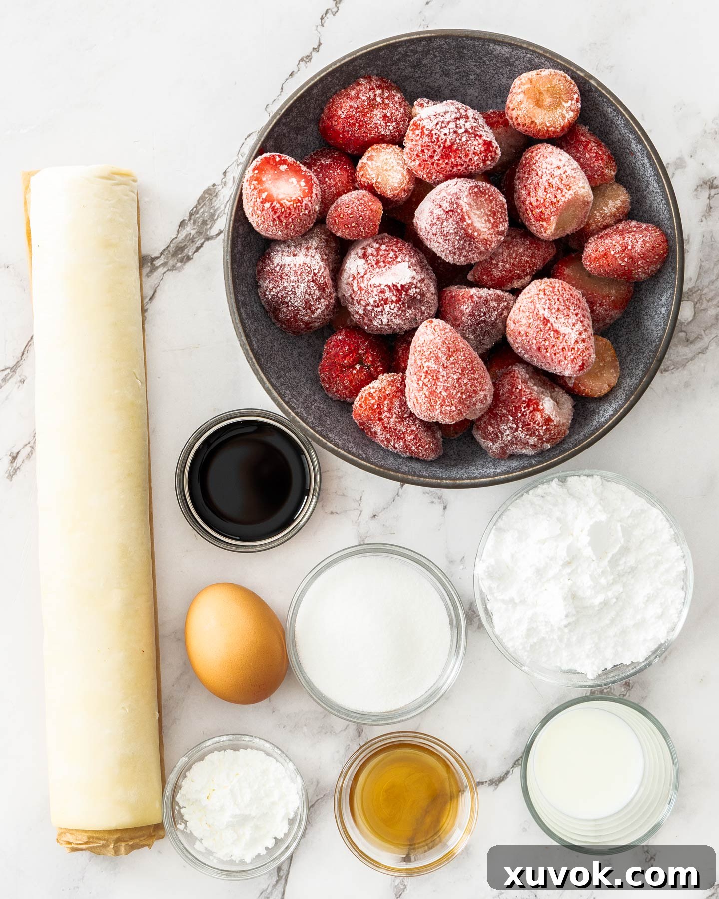 A curated display of fresh ingredients for strawberry turnovers, including vibrant red strawberries, golden puff pastry sheets, and granulated sugar, artfully arranged on a pristine marble surface.