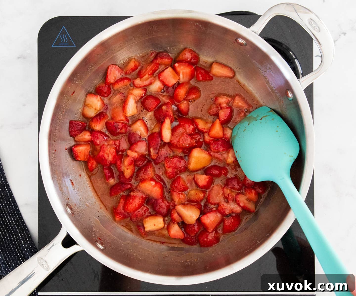 Fresh strawberries simmering gently in a saucepan, surrounded by their rich, red liquid as they begin to break down, forming the delicious filling.