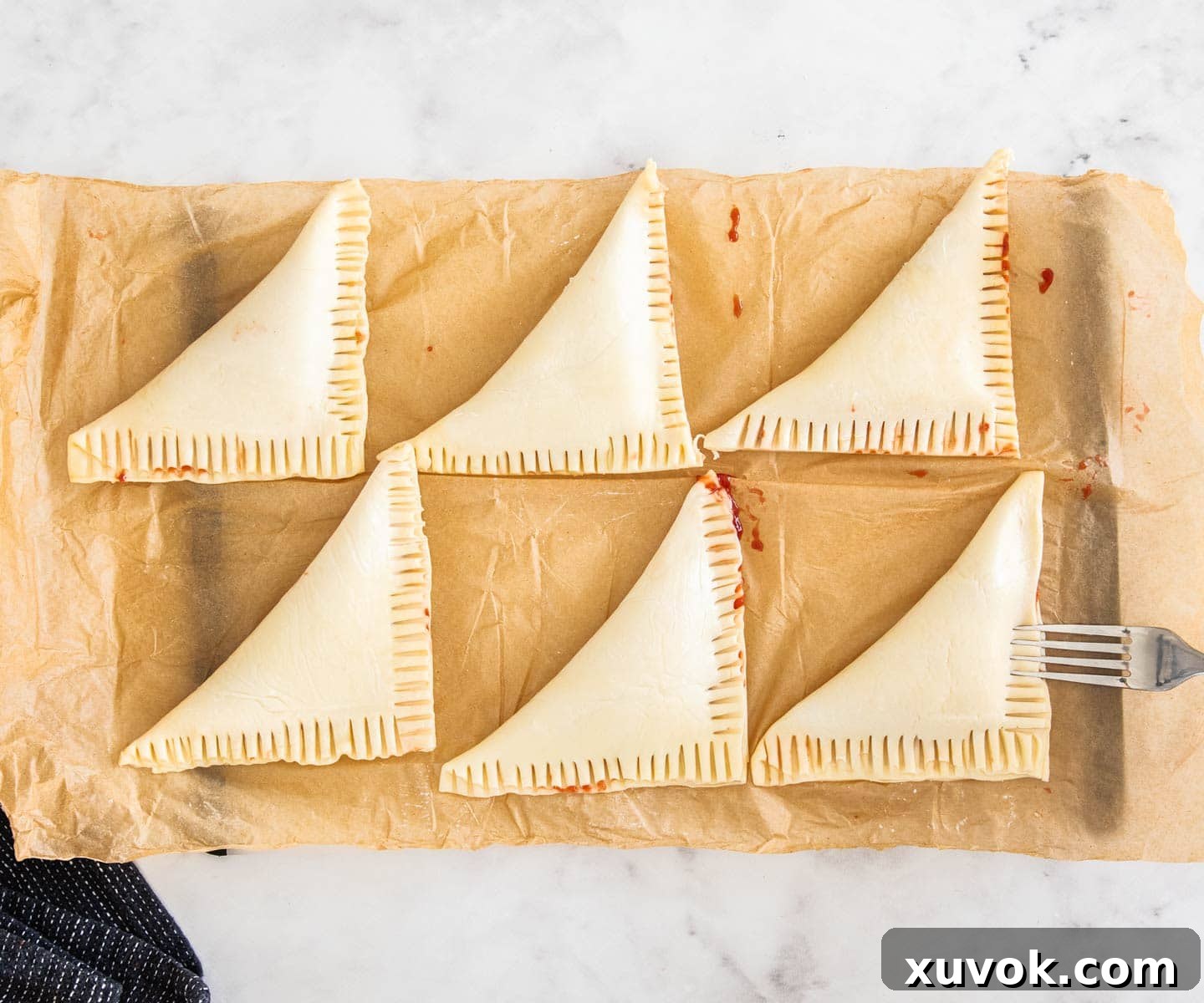 Six perfectly folded triangular pastry turnovers, with the strawberry filling securely sealed inside, featuring decorative fork-crimped edges.