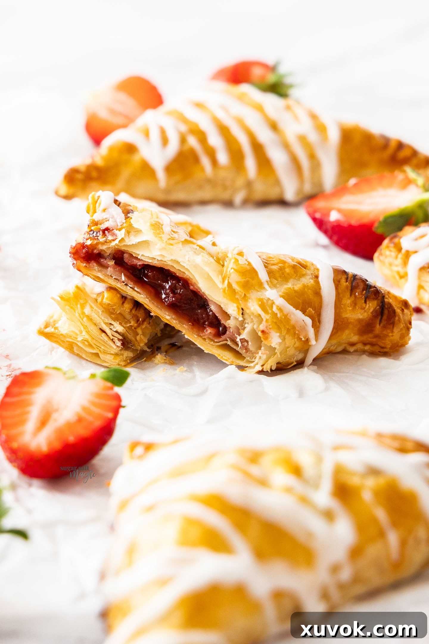 A perfectly baked strawberry turnover, artfully sliced in half, revealing the vibrant, thick red strawberry filling contrasted by the delicate, flaky layers of the puff pastry.