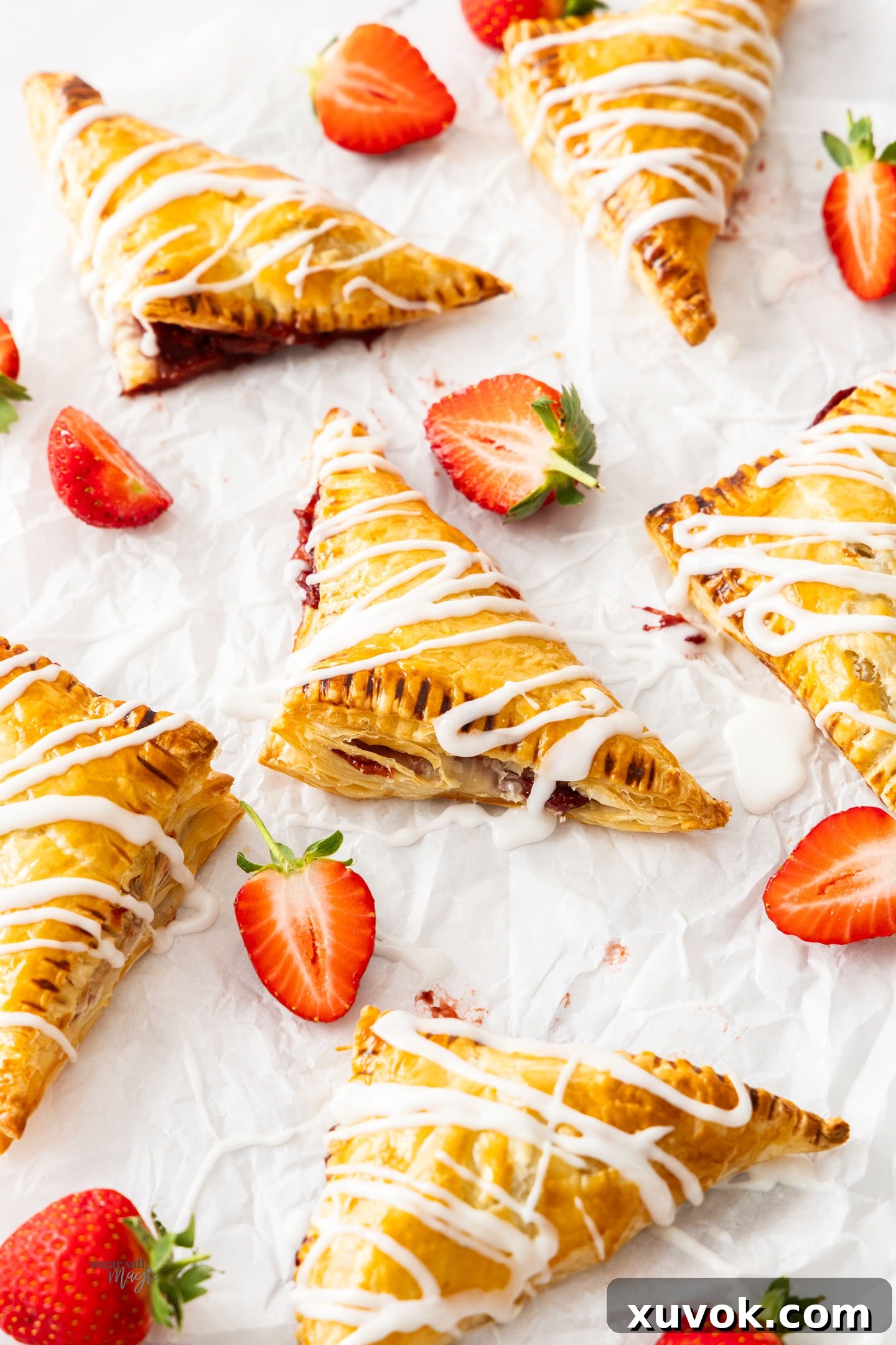 Six perfectly baked, golden-brown strawberry turnovers, beautifully puffed and crisp, arranged neatly on a sheet of baking parchment paper.