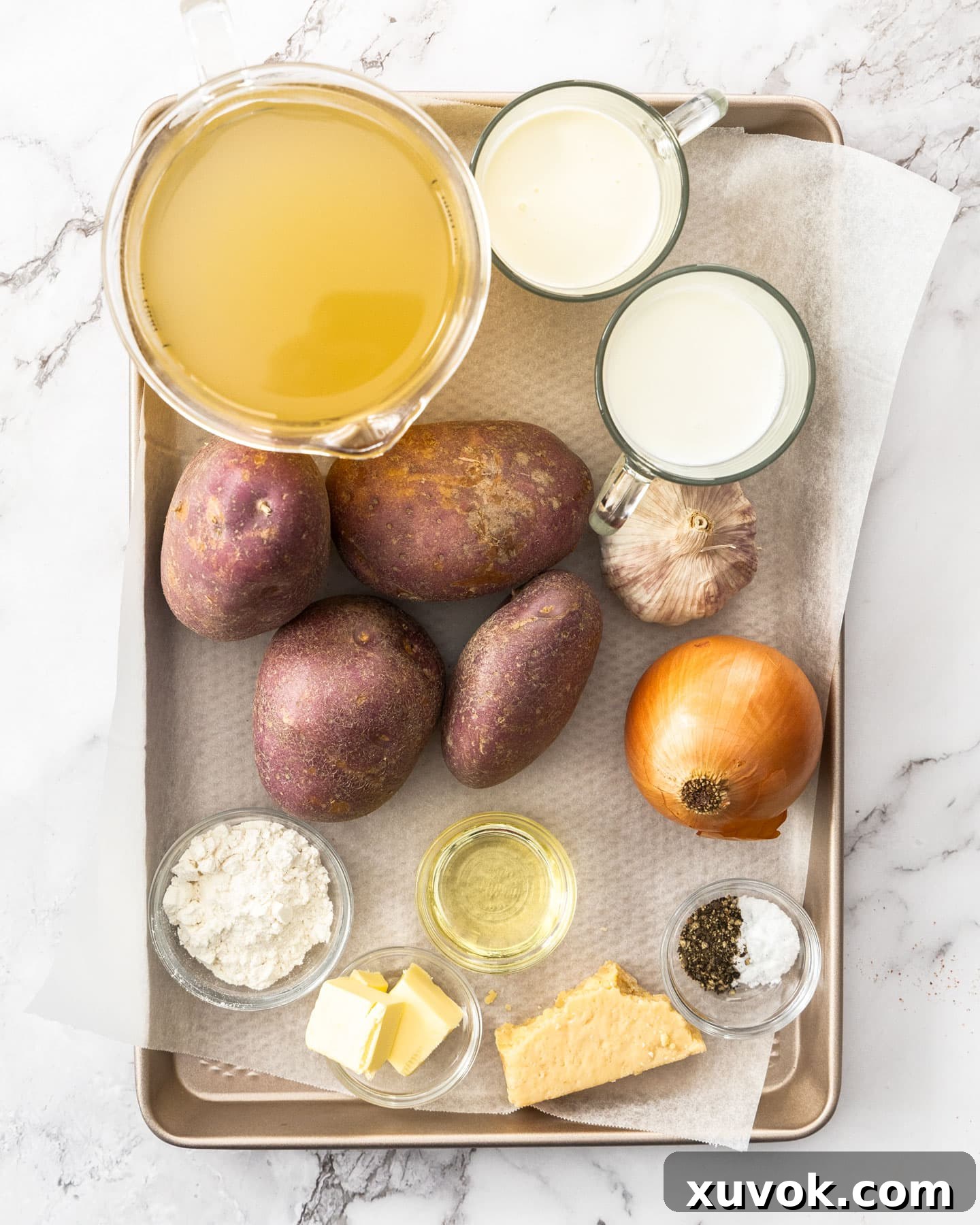 A selection of fresh ingredients including garlic, potatoes, onion, and herbs laid out on a baking tray, ready for cooking.