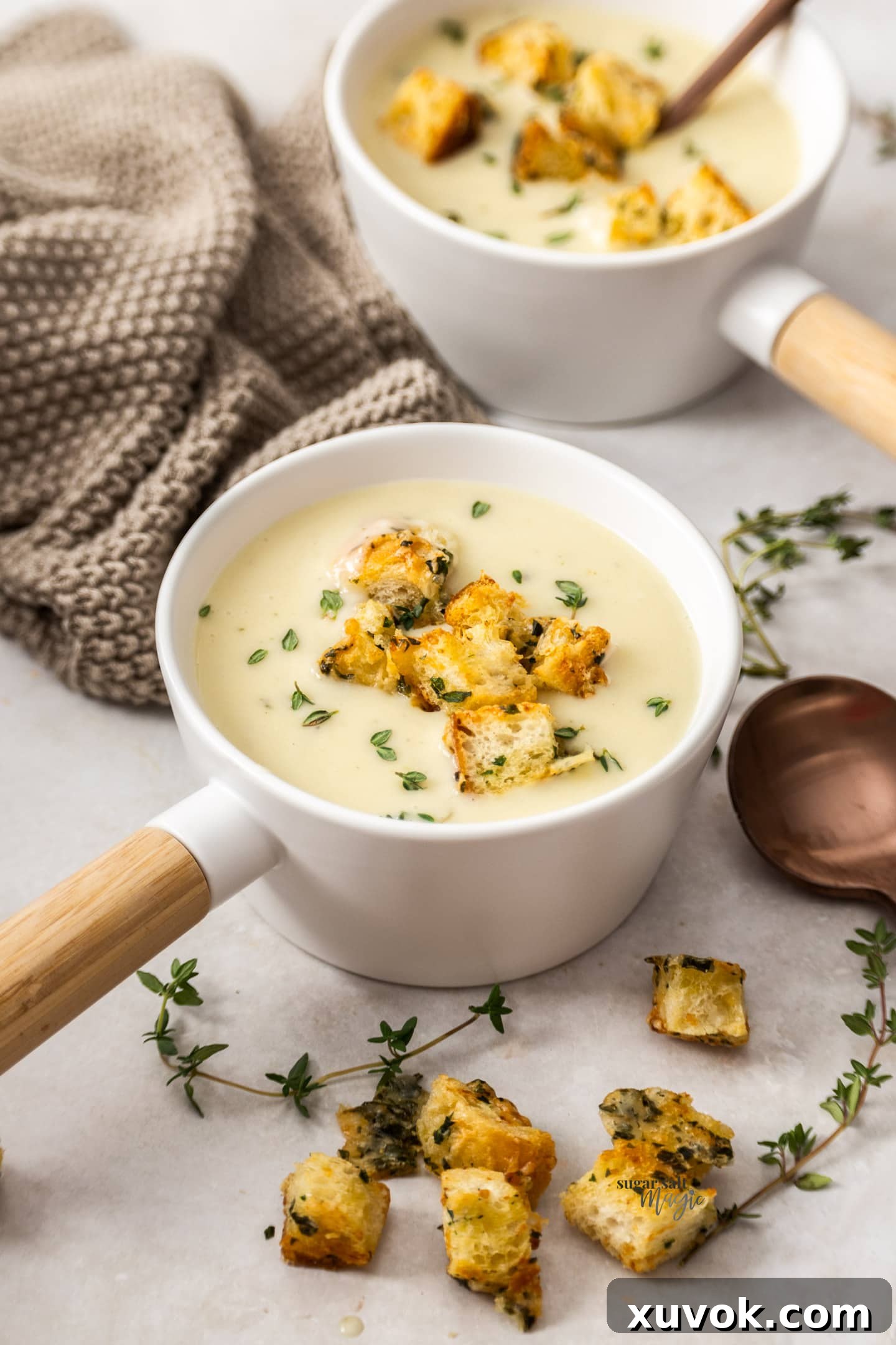 Two soup bowls filled with creamy roasted garlic potato chowder, garnished with crispy croutons and fresh herbs.