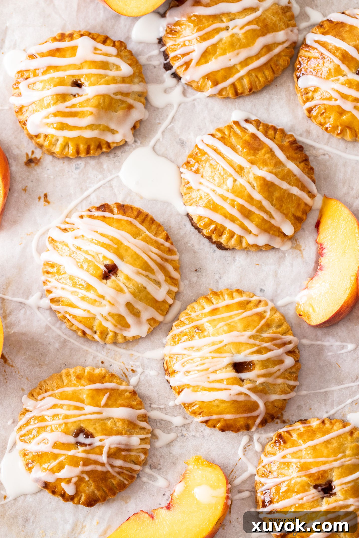 A vibrant top-down view of perfectly round peach hand pies, freshly baked and glistening with a sweet white glaze.