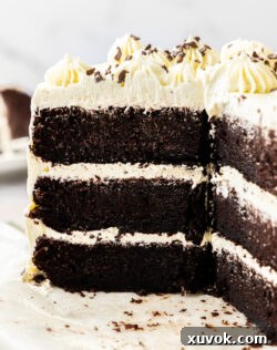 A three-layer chocolate cake with vanilla buttercream on a platter, with a few slices already cut and served.