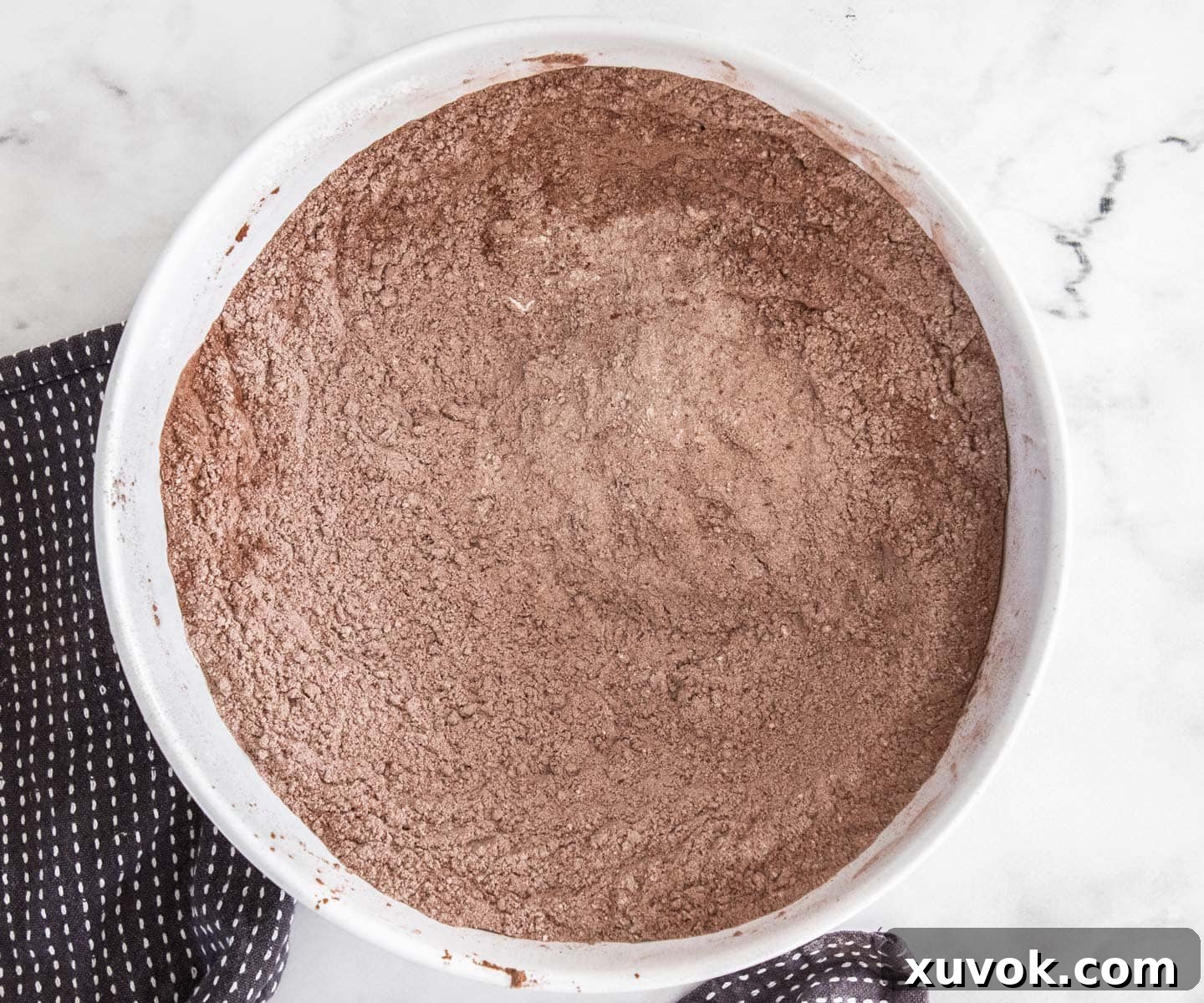 Close-up of flour, cocoa, and other dry ingredients mixed together in a large mixing bowl, ready for the wet ingredients.