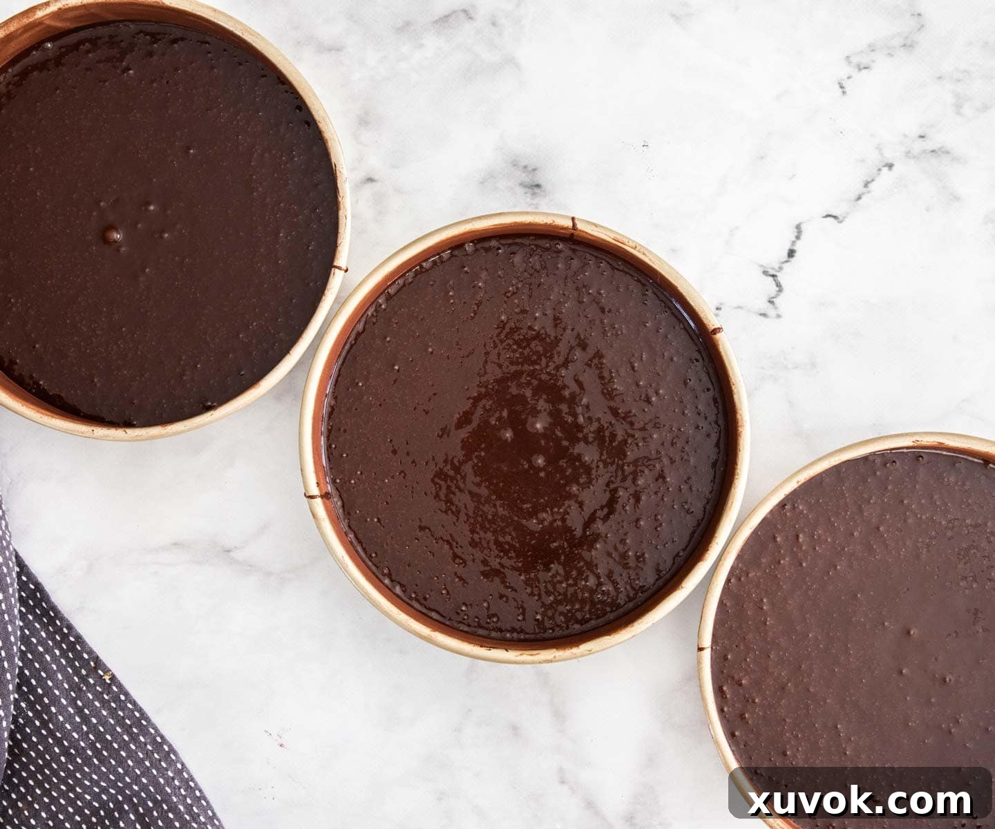 Chocolate cake batter evenly divided into three 8-inch round cake pans, ready for baking.