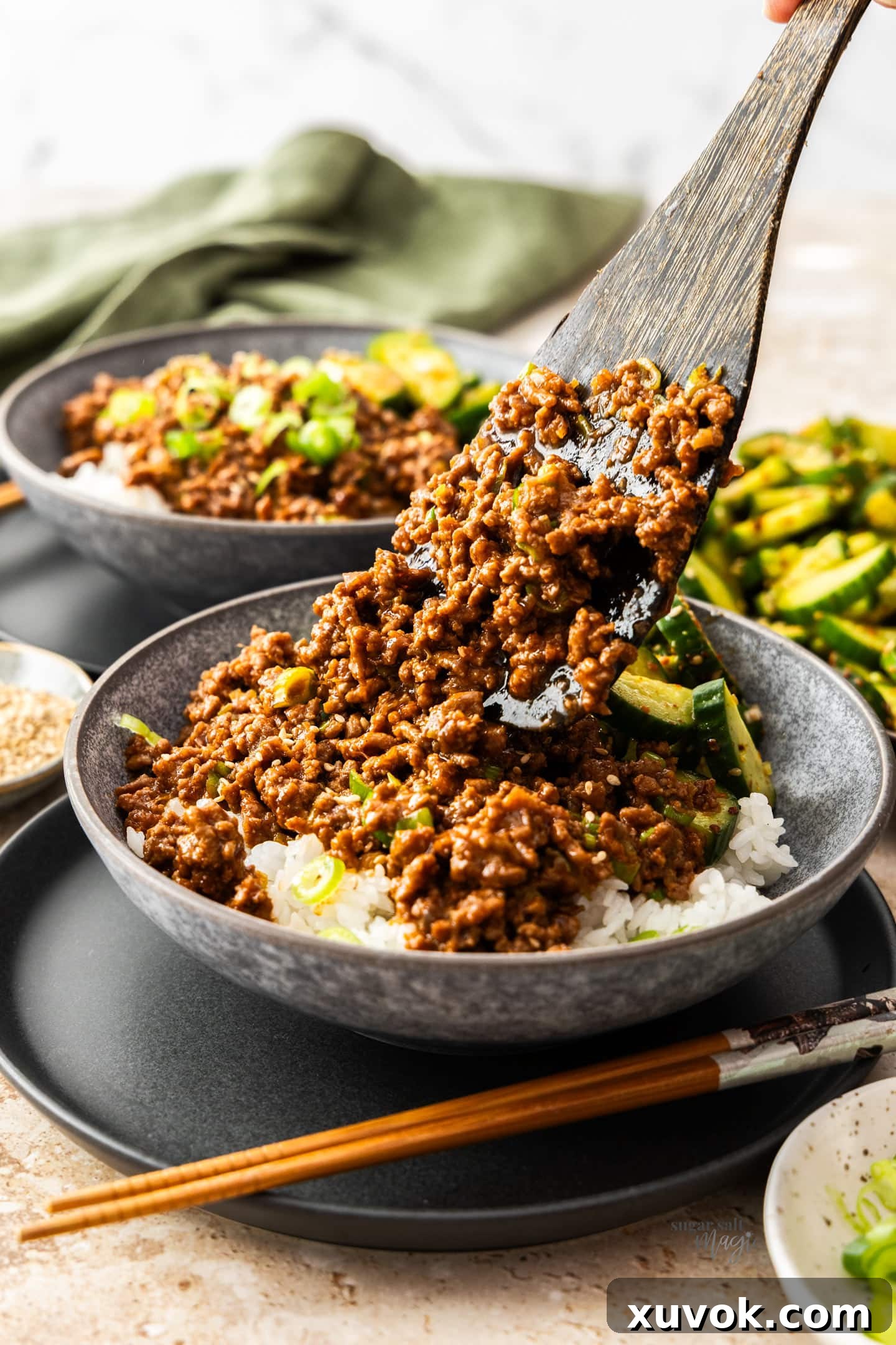 A spatula placing gochujang beef into a bowl over rice.