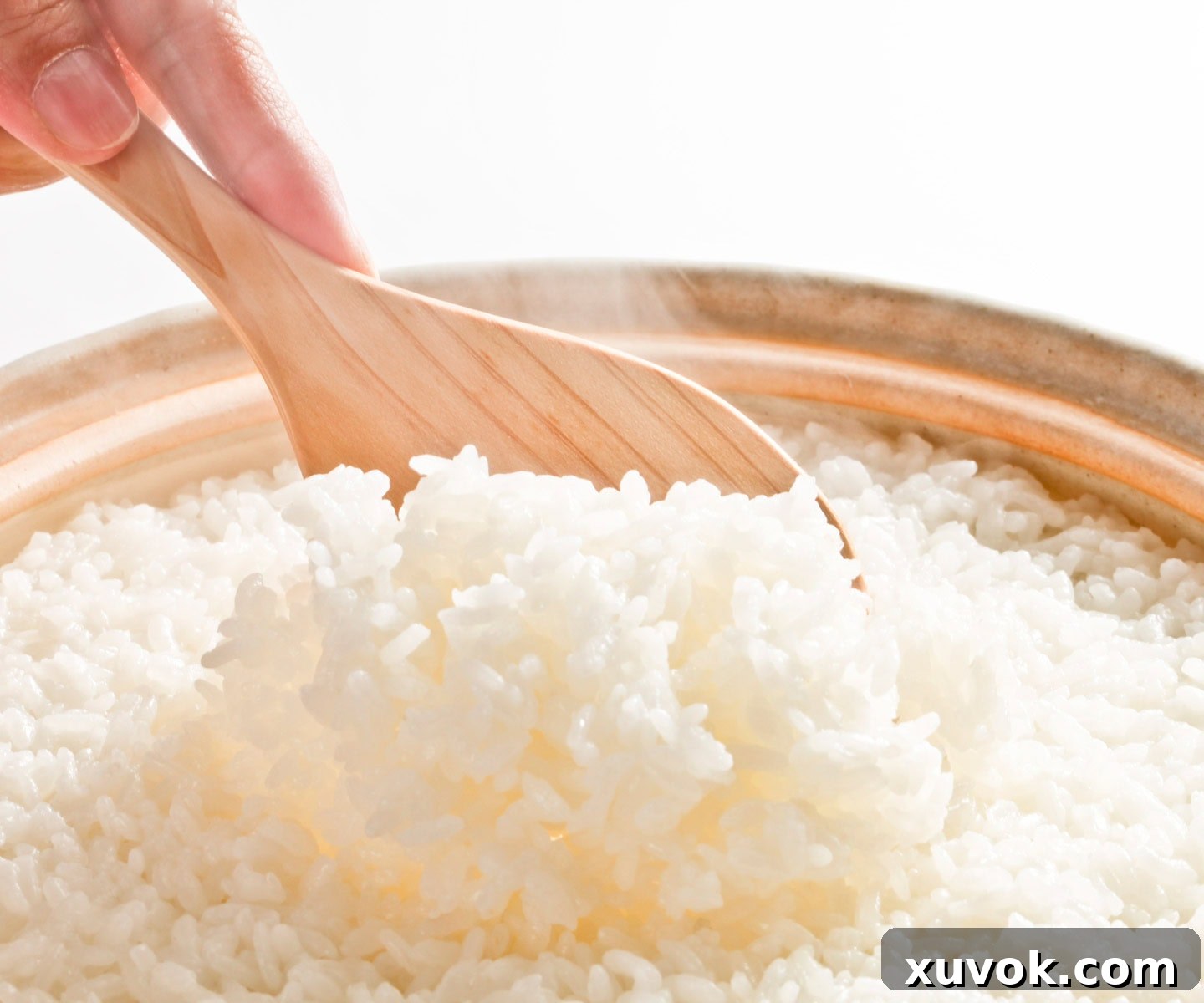 Freshly cooked rice, steaming and being fluffed with a spoon.
