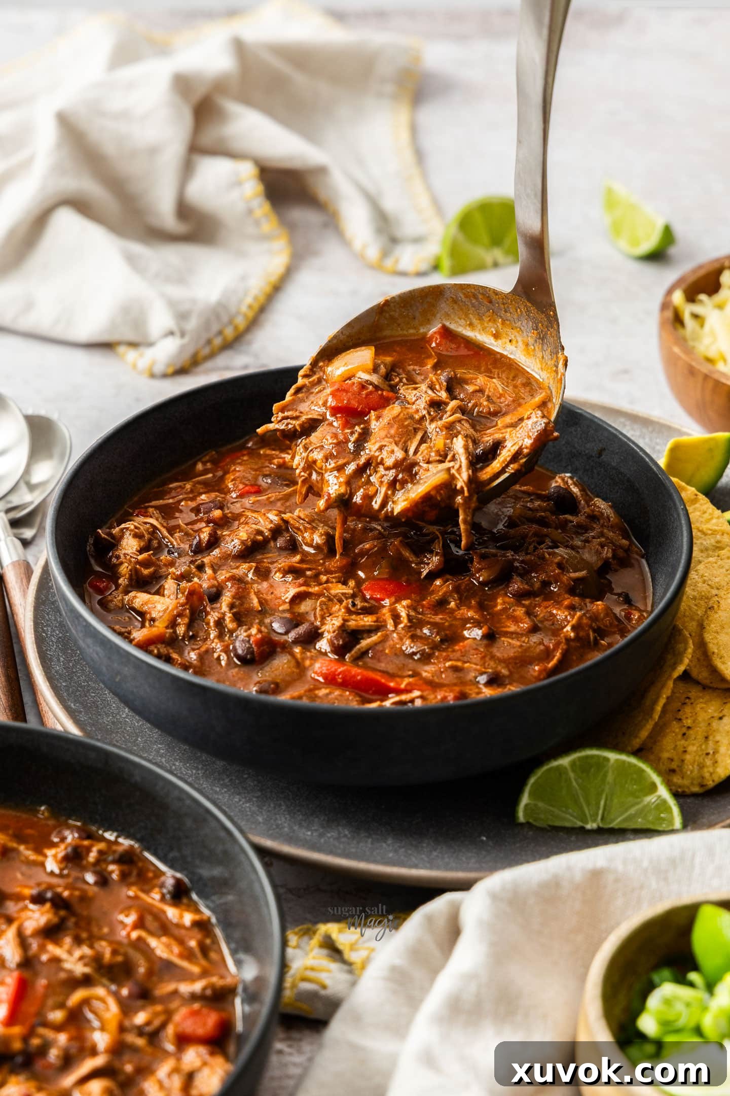 A ladle pouring rich slow cooker chilli con carne into a dark bowl, highlighting its comforting nature.