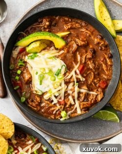 Top down view of a bowl of chilli con carne topped with avocado, sour cream and cheese.