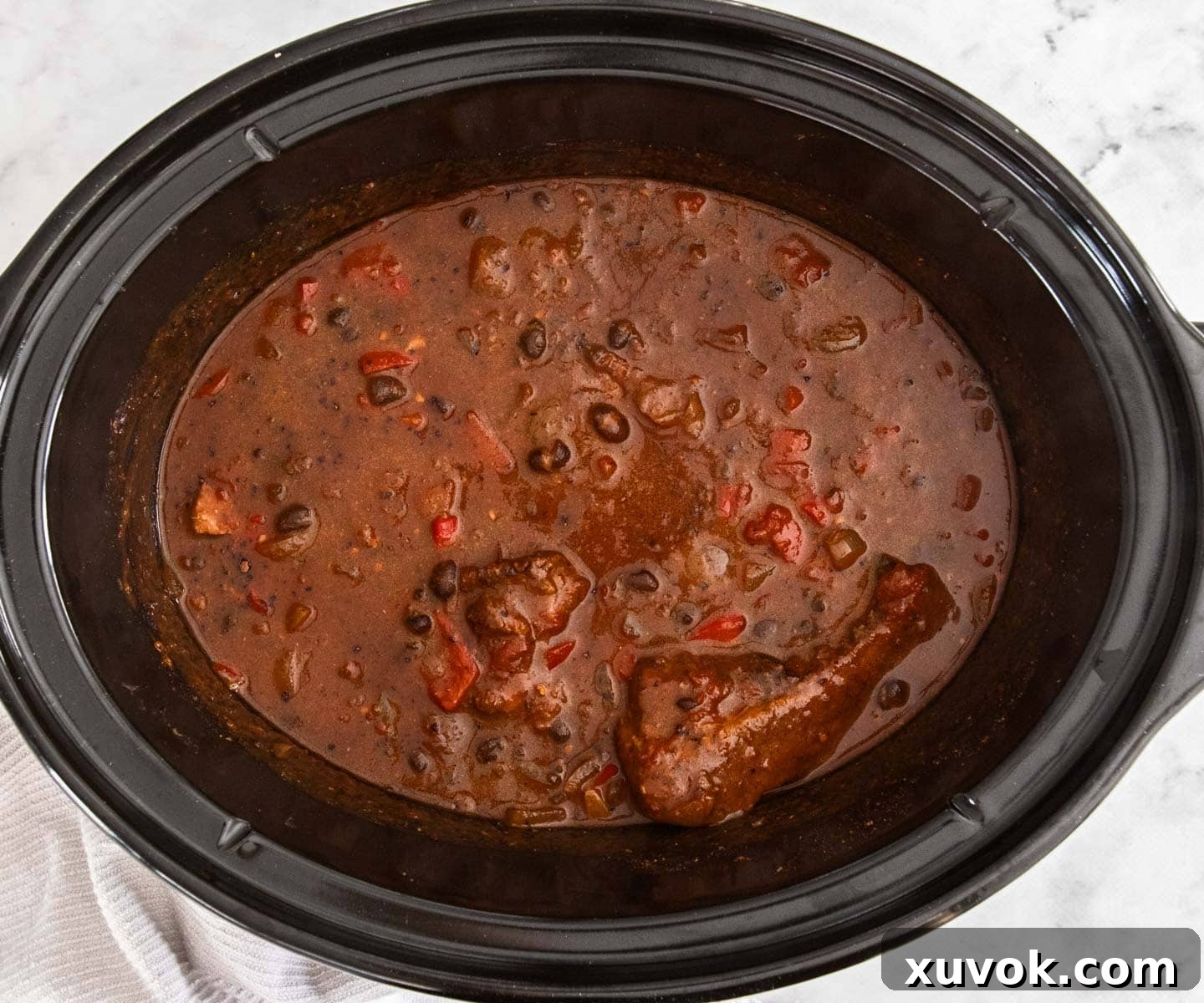 The chilli con carne in the slow cooker, with black beans freshly stirred in, showing a rich, dark color.