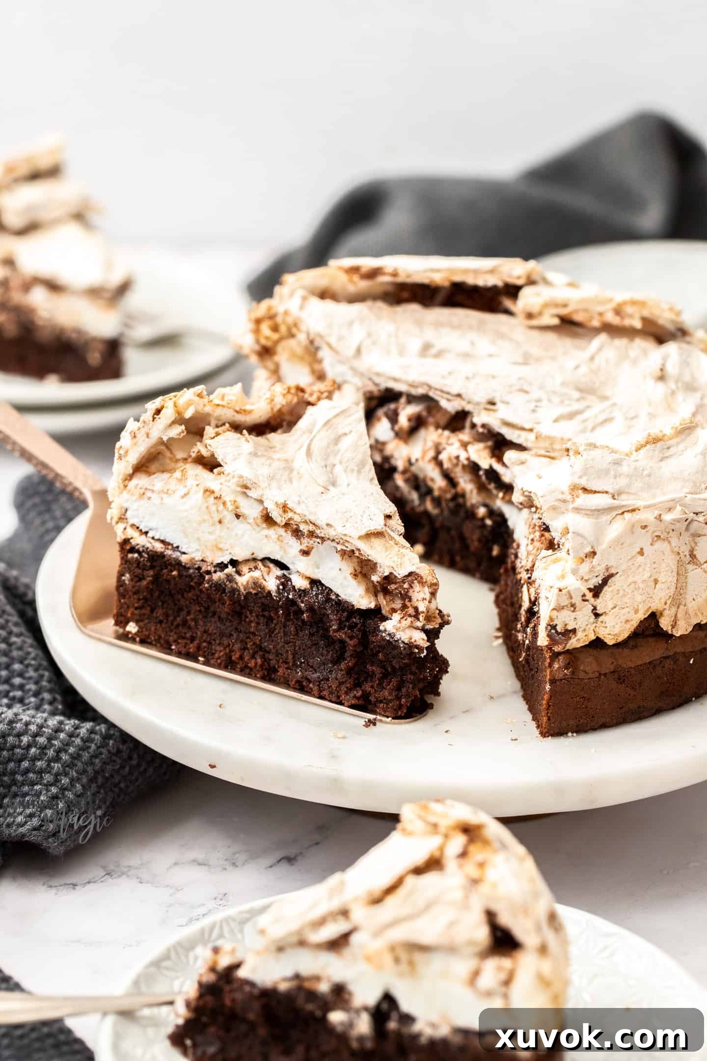 A perfectly sliced piece of Chocolate Meringue Brownie Cake, revealing its distinct layers of rich brownie and fluffy meringue, presented on a pristine white marble platter.