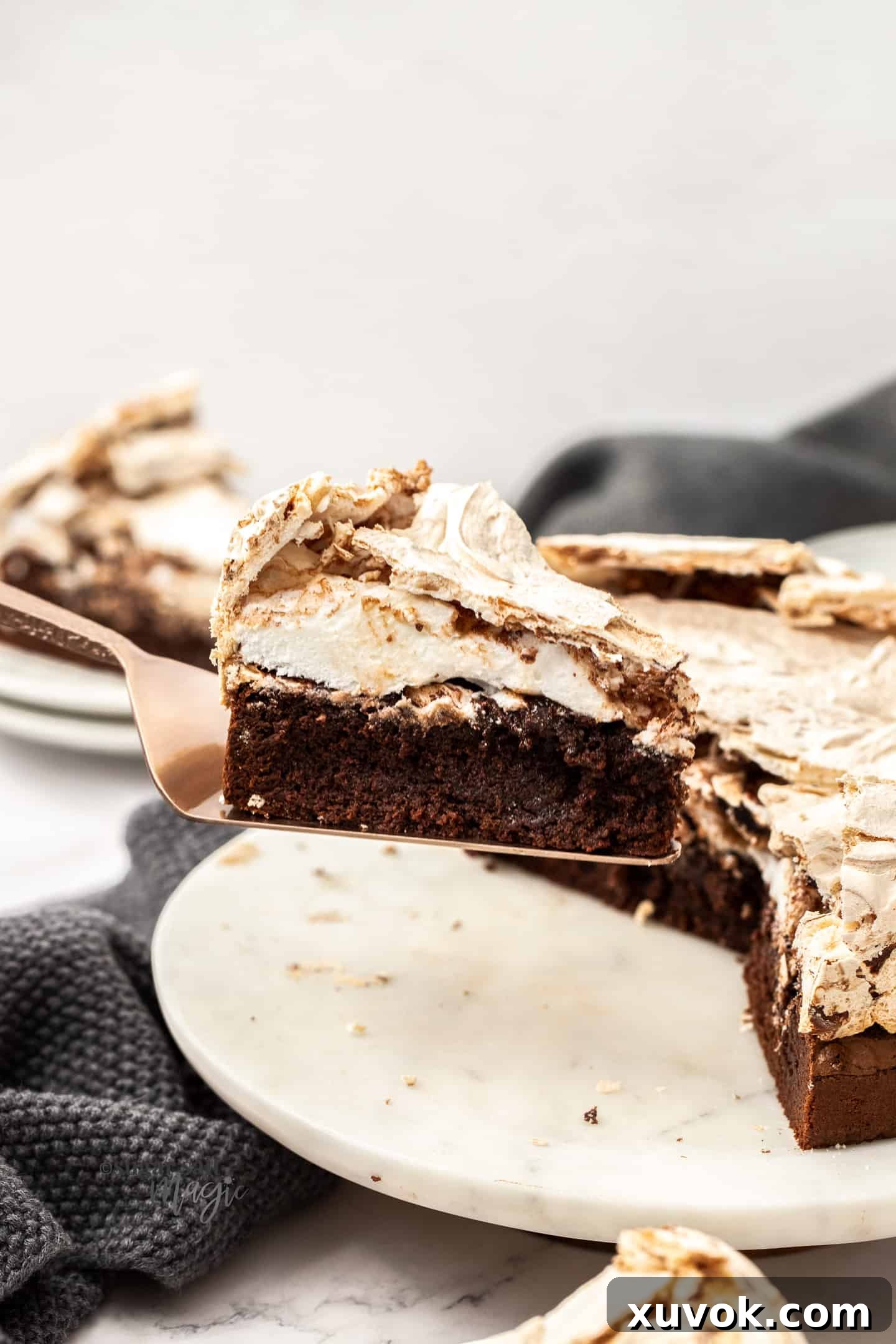 A perfectly portioned slice of Chocolate Meringue Brownie Cake, delicately held on a bronze cake slice, invitingly presented towards the camera.