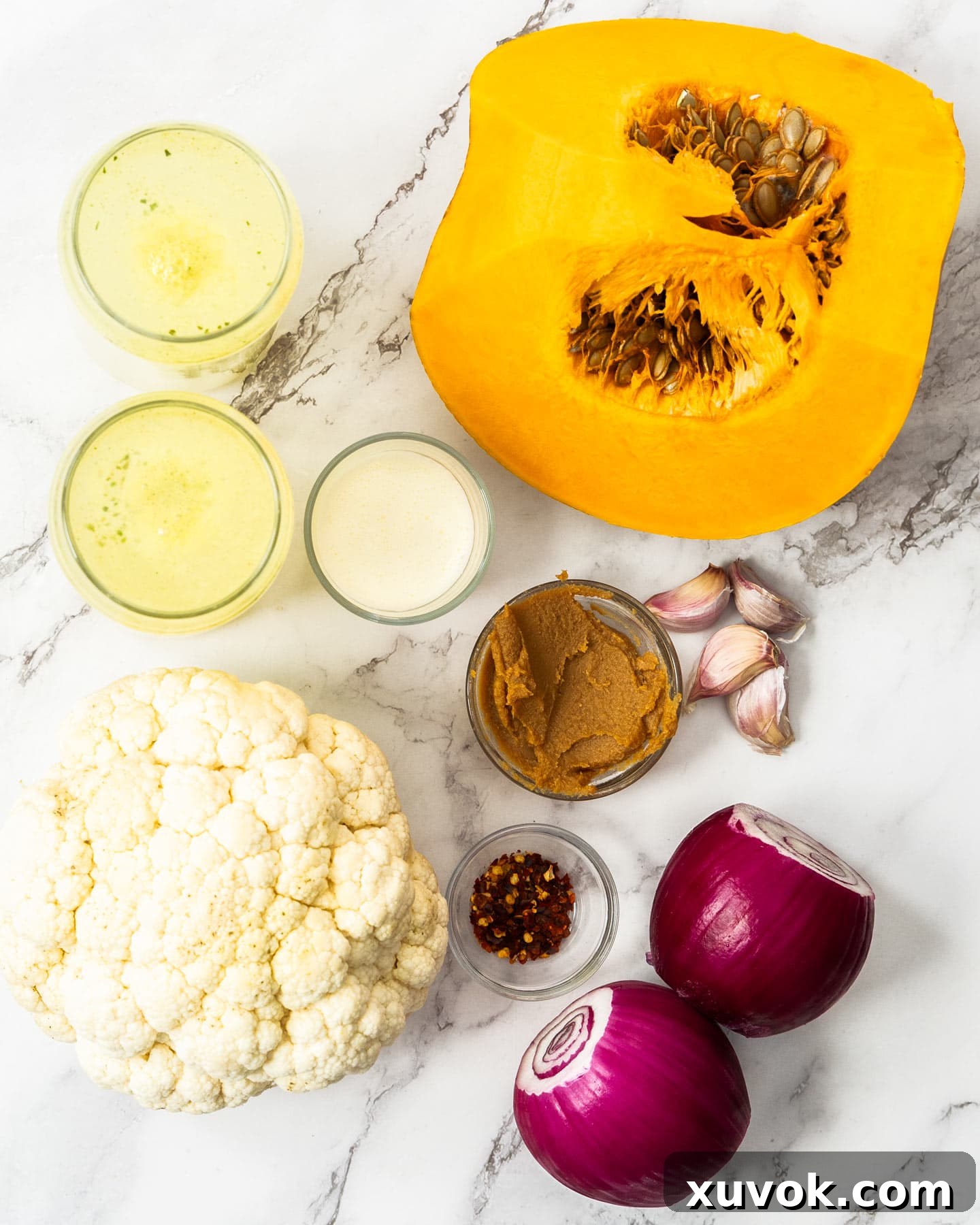 Fresh ingredients for pumpkin and cauliflower soup laid out on a marble surface, including pumpkin, cauliflower, onions, garlic, and miso paste.