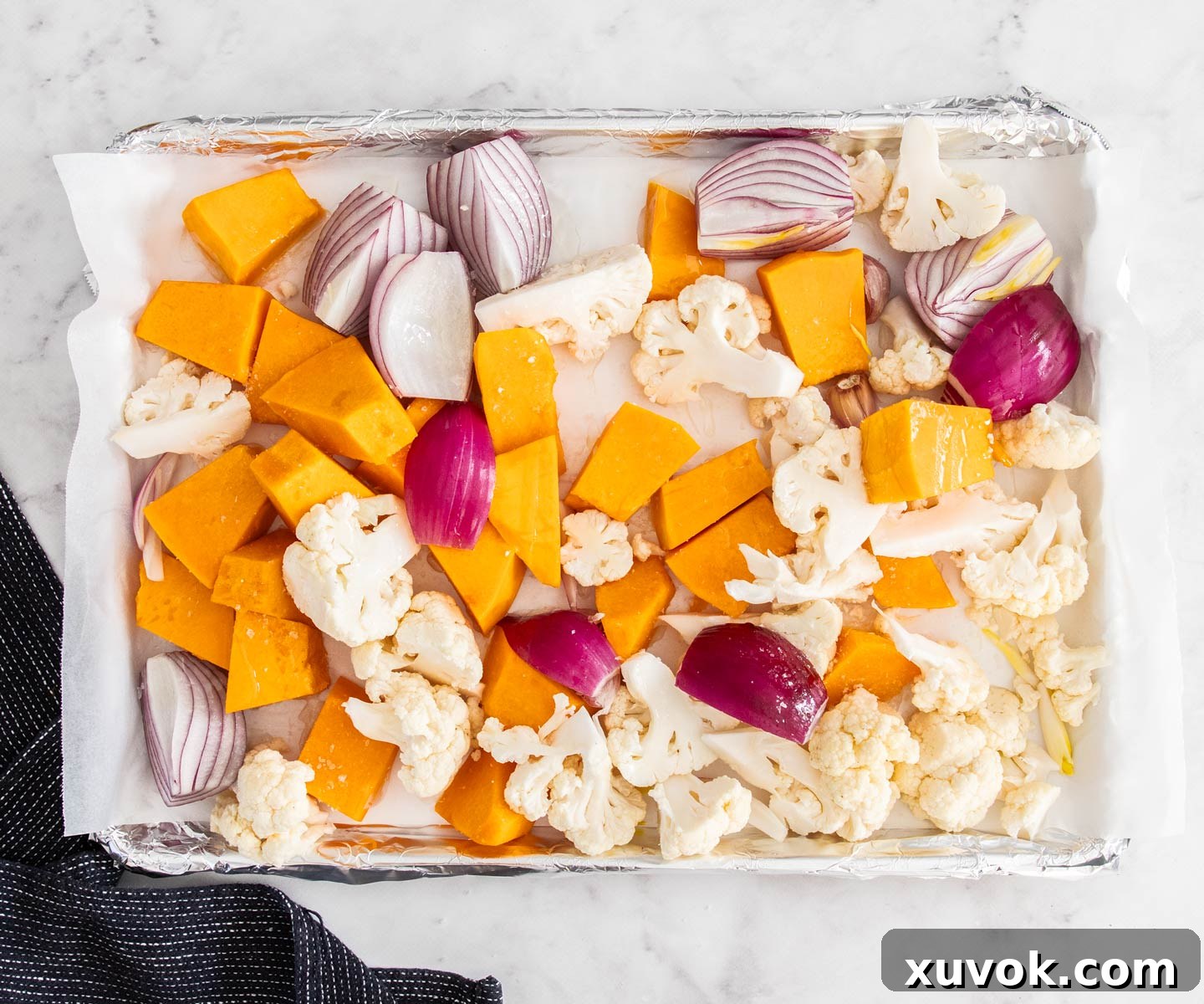 Pumpkin, cauliflower, and red onions prepared and seasoned on a baking pan, ready for roasting.