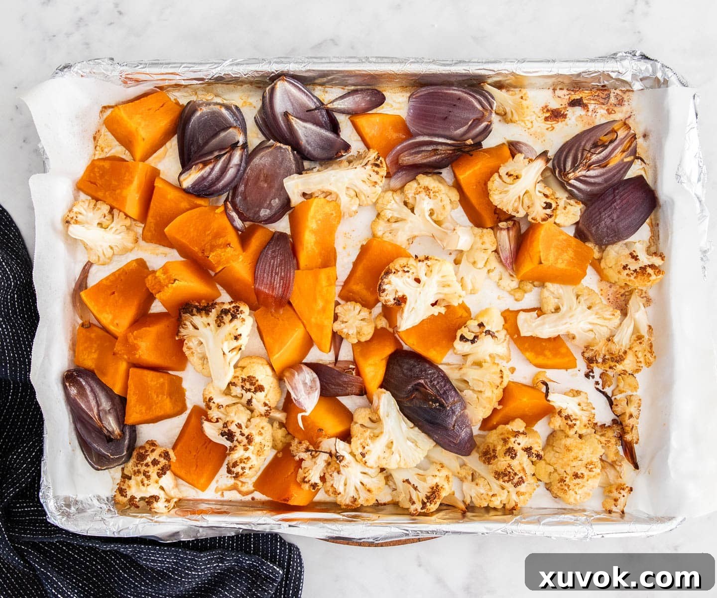 A baking pan filled with perfectly roasted pumpkin, cauliflower, onions, and garlic, showing golden-brown caramelization.