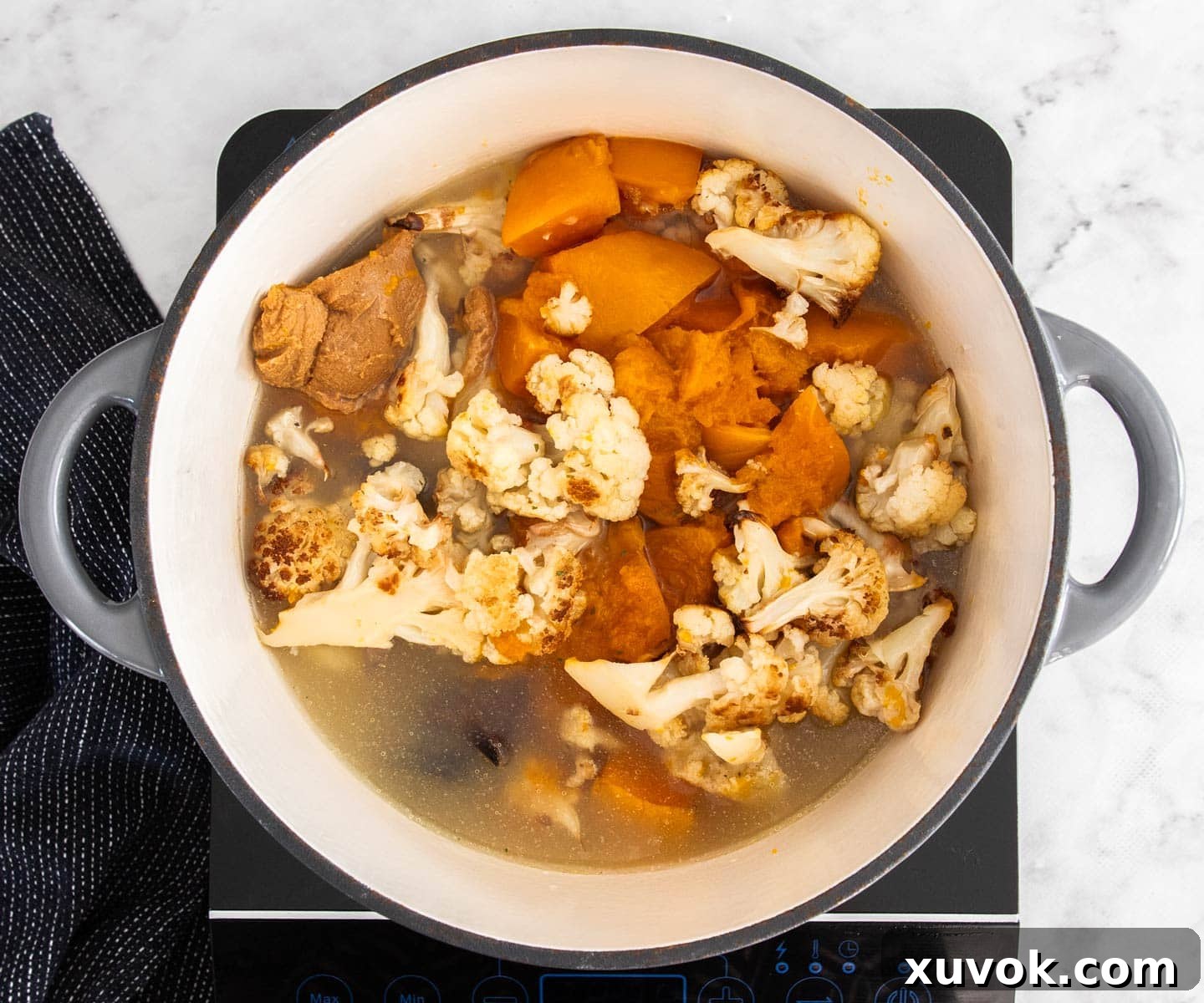 Roasted cauliflower and pumpkin in a Dutch oven, with added stock and miso paste, ready for blending.