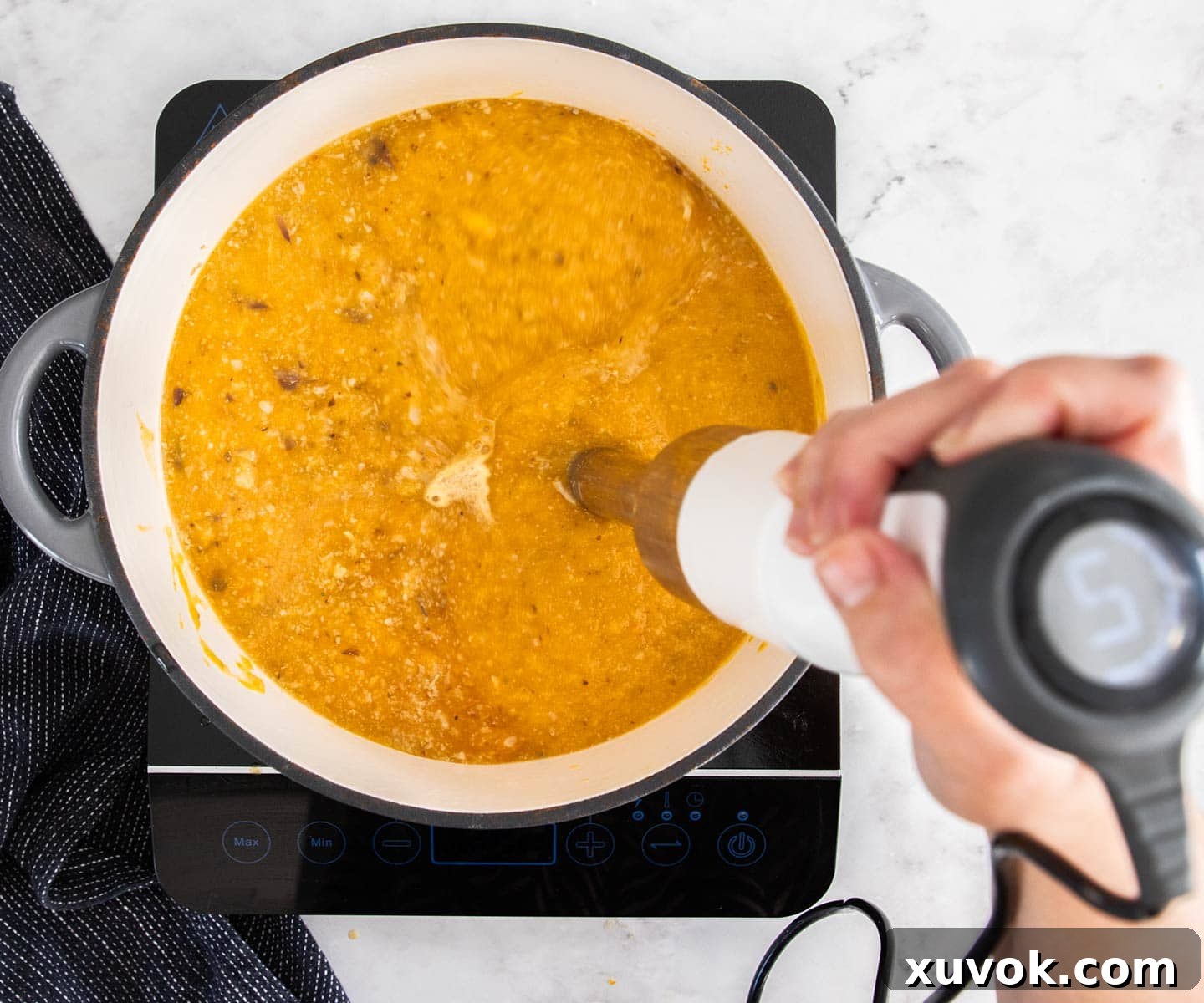 A stick mixer blending pumpkin soup in a Dutch oven, creating a smooth, creamy texture.