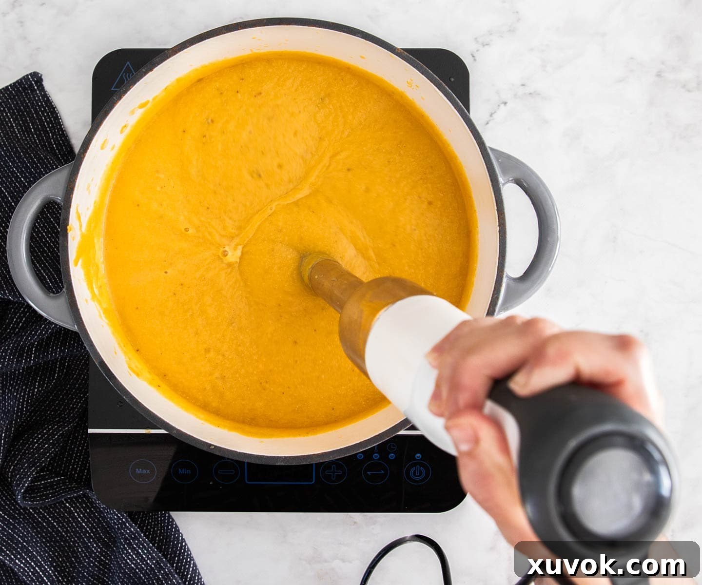 Pumpkin soup in a pan being blended with a stick blender for a smooth finish.