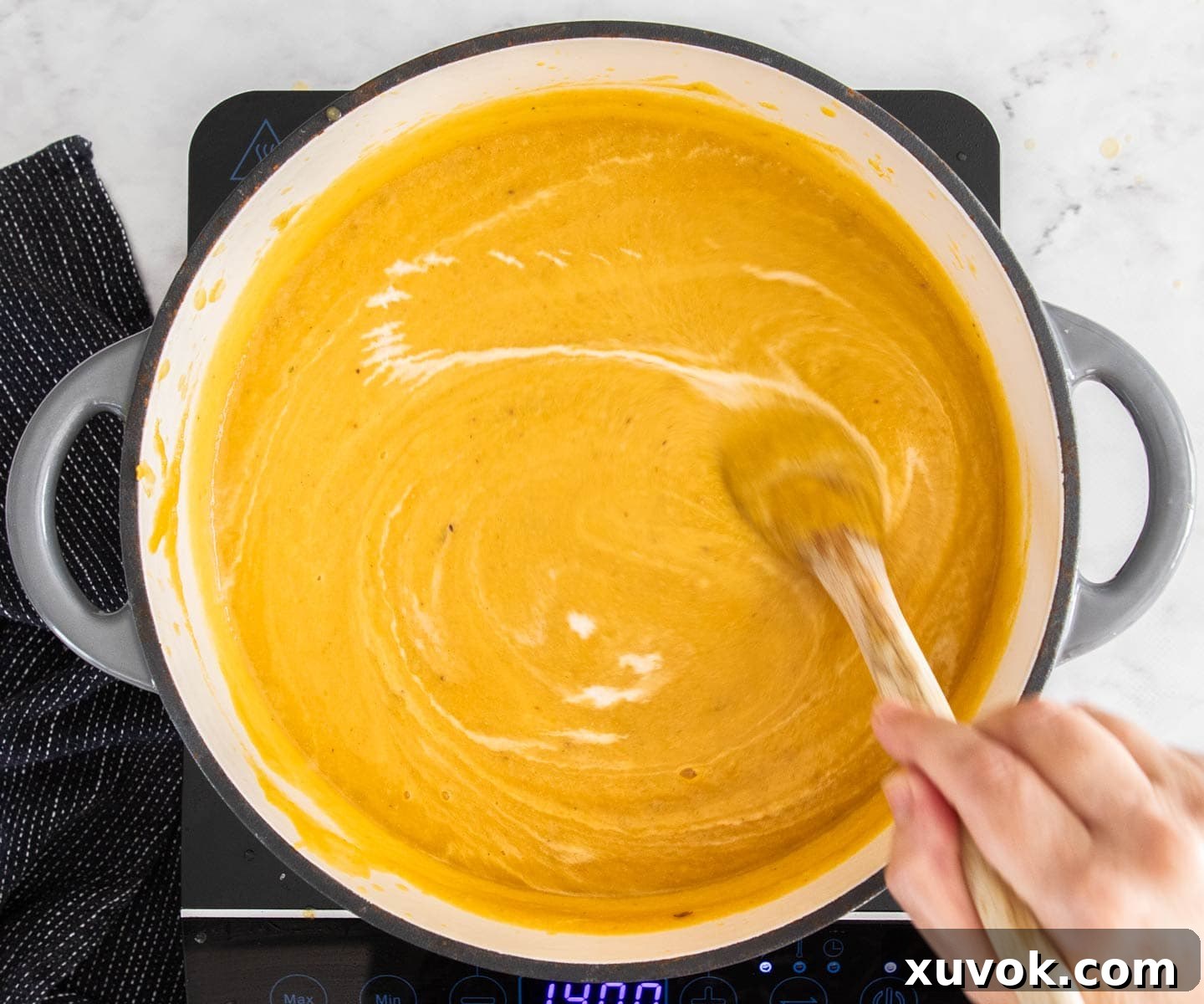A rich, creamy pumpkin soup being stirred in a pot after cream has been added, creating a beautiful swirl.