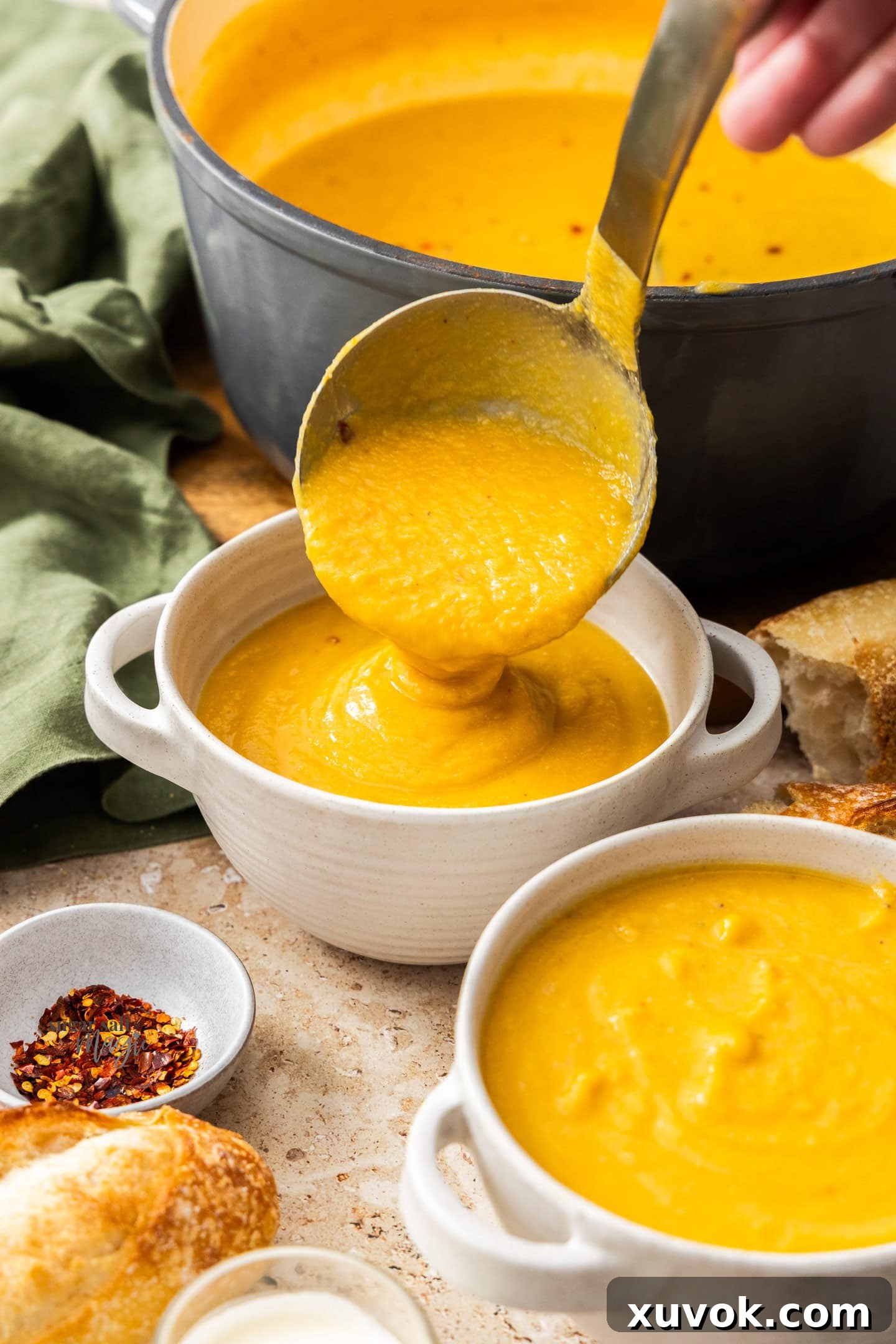 A ladle pouring creamy cauliflower pumpkin soup into a rustic bowl, ready for garnishing.