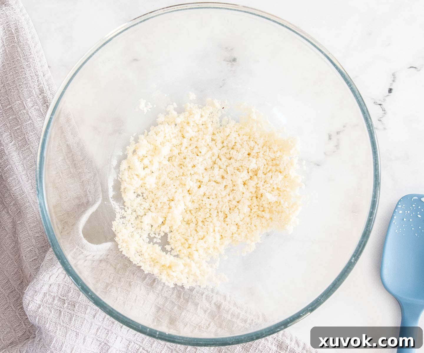 A bowl of crumbs soaked in milk next to a blue spatula.