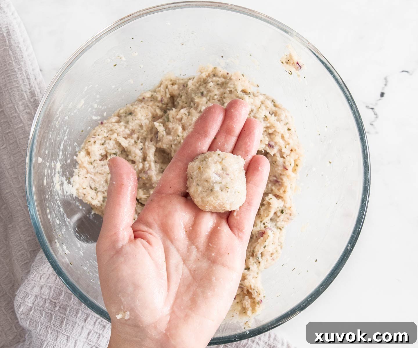 A person holding a ball of chicken mince over a bowl.