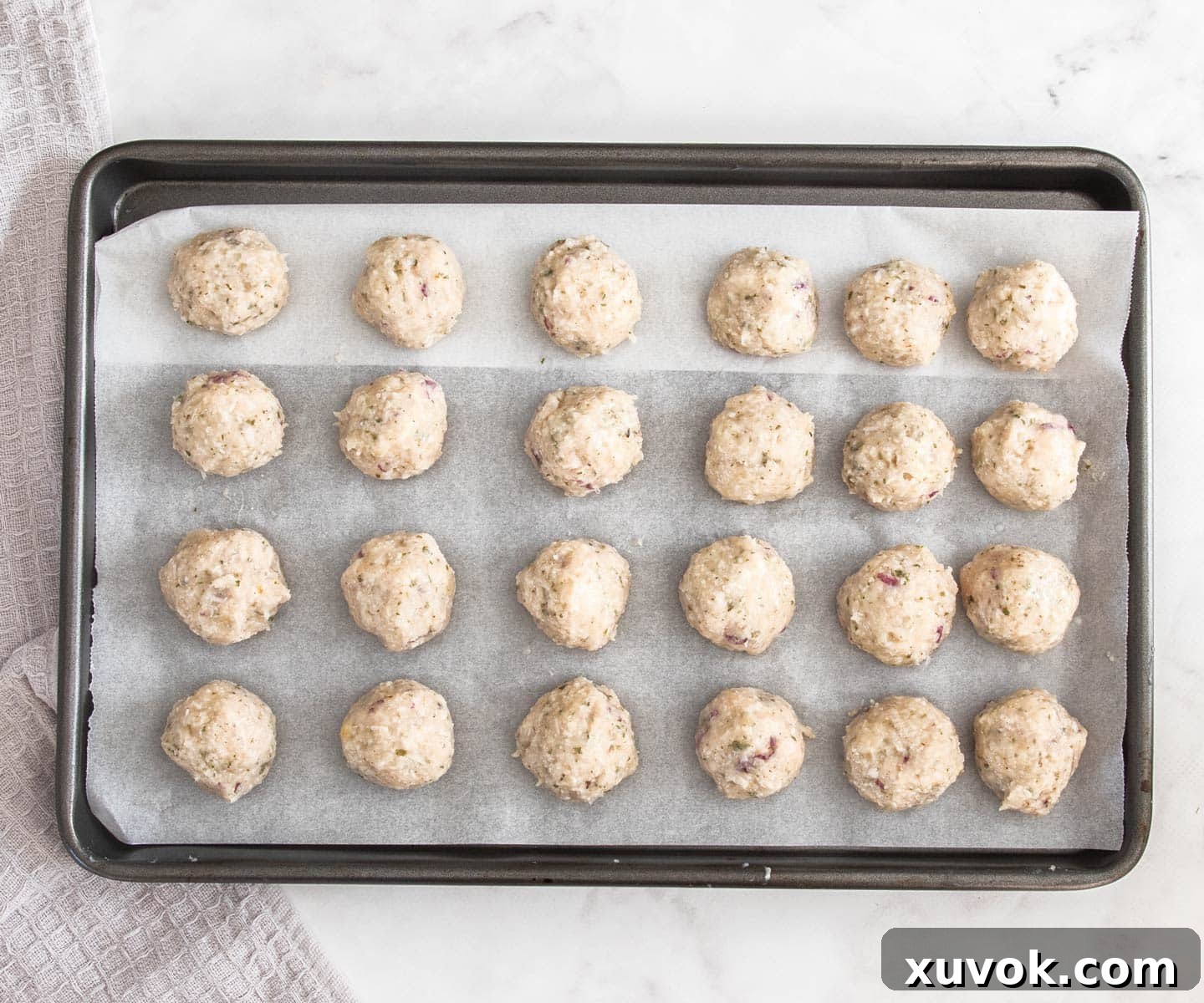 A baking sheet filled with raw chicken meatballs on top of a marble surface.
