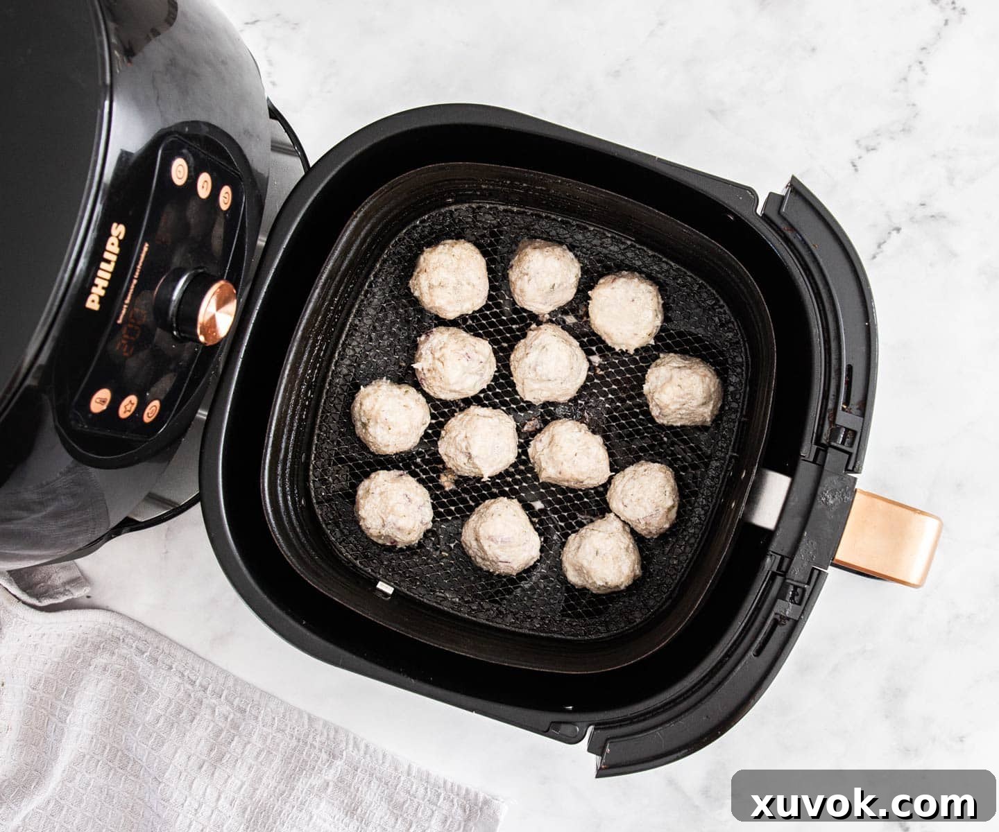 A black air fryer with balls of meat in it before cooking.
