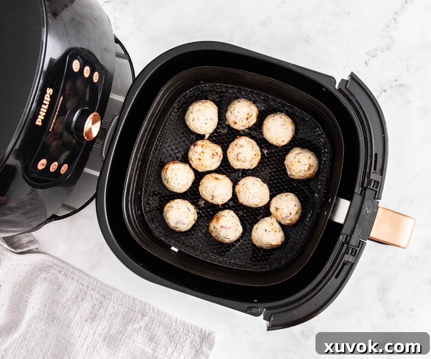 A black air fryer with balls of meat in it, partially cooked.