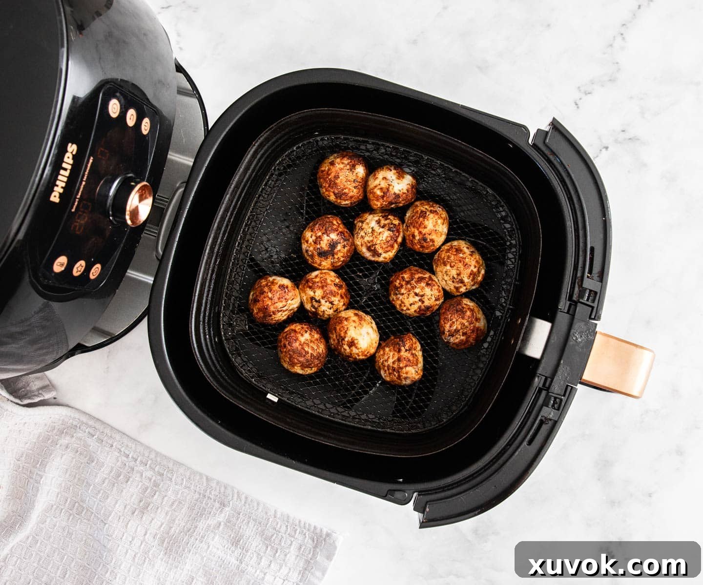 A black air fryer with some meatballs in it, fully cooked.