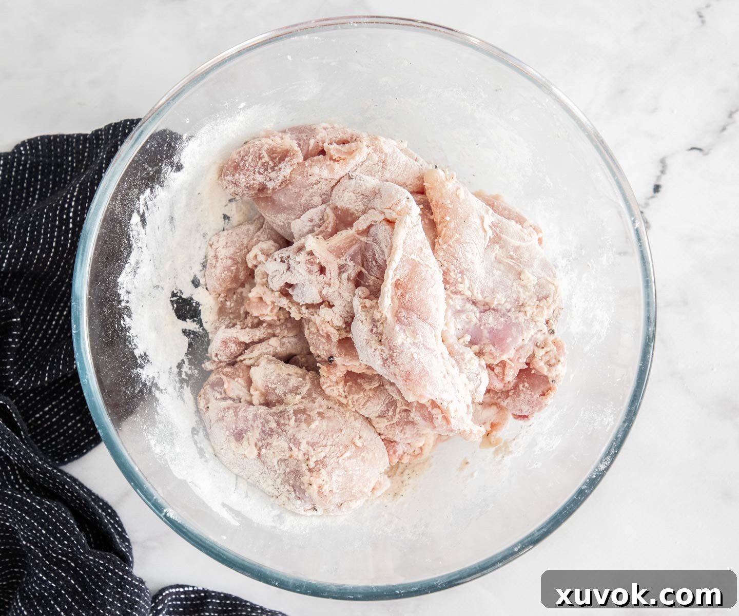 Chicken thighs dusted with flour and seasoning in a bowl, ready for cooking.