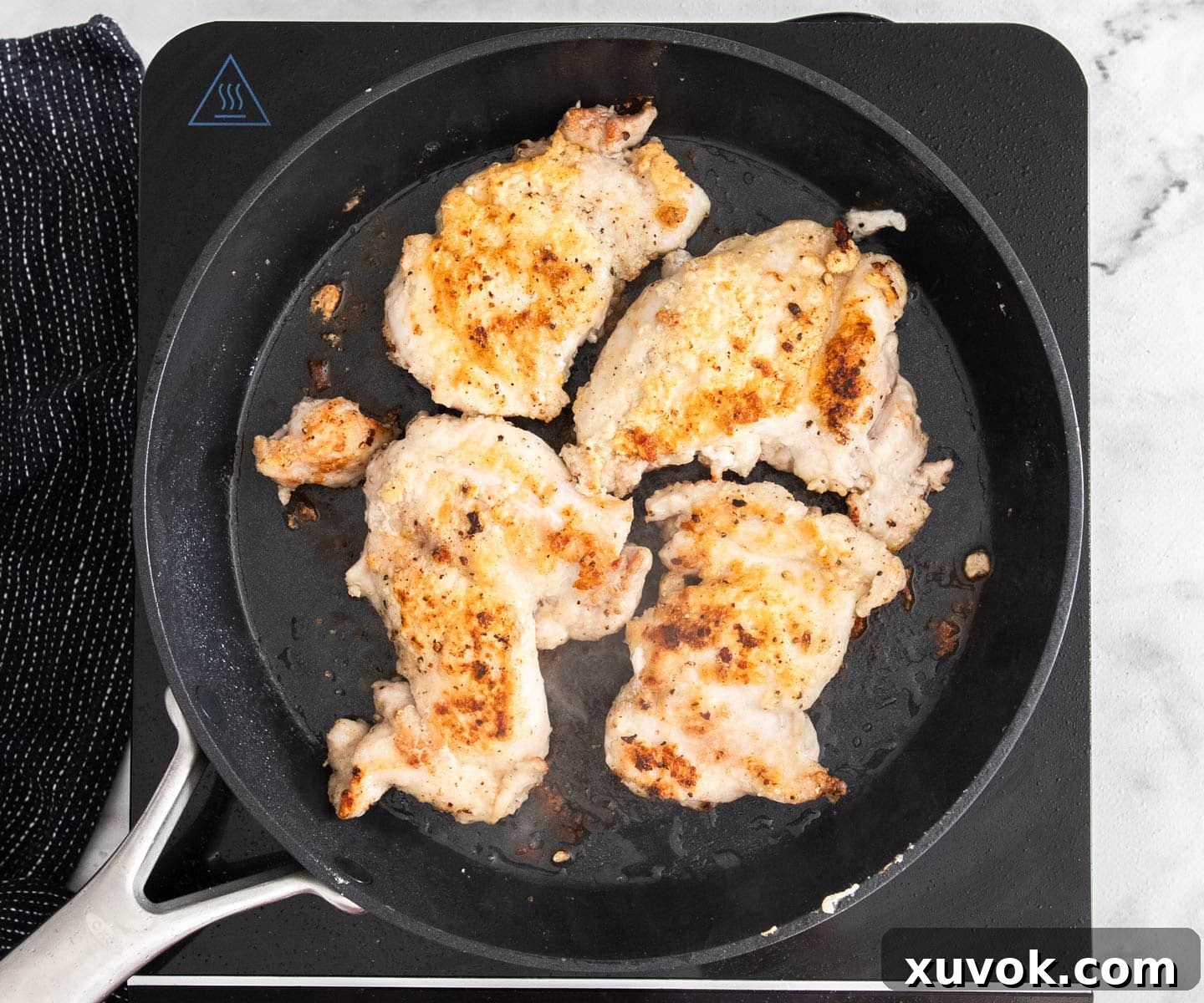 Four pieces of flour-dusted chicken browning in a frying pan.