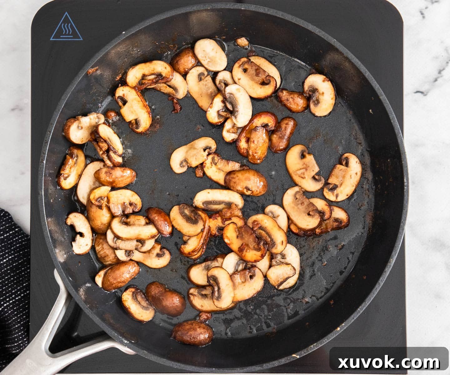 Sliced mushrooms sautéing in a frying pan until golden.
