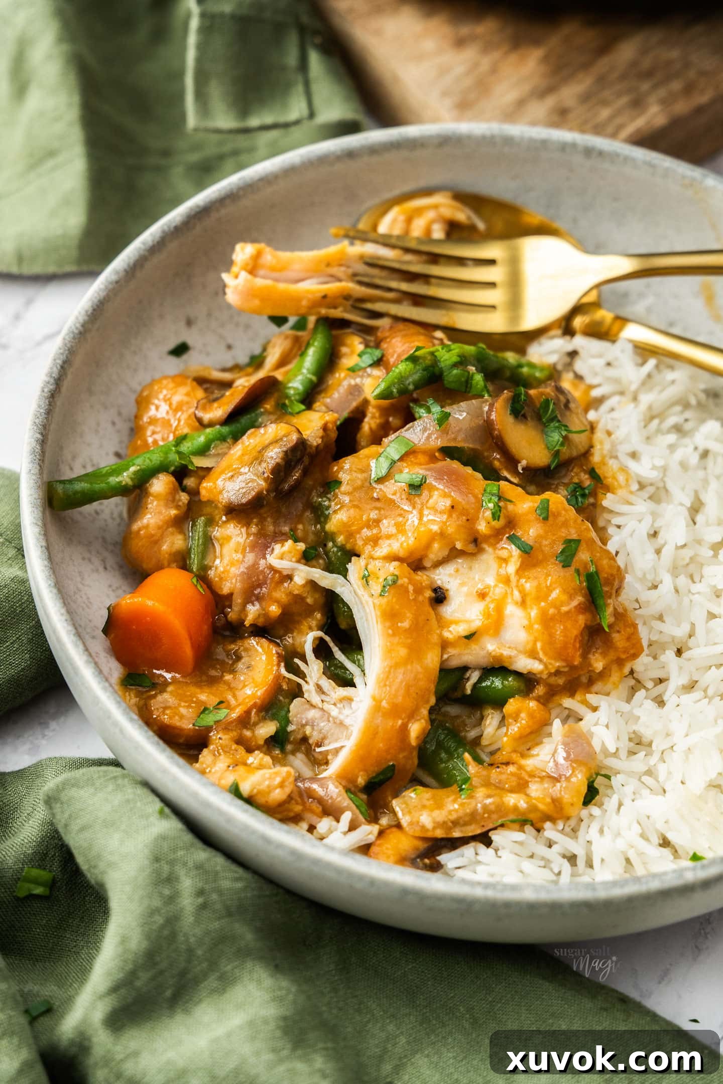 Slow cooker apricot chicken next to rice in a bowl, garnished with fresh herbs, ready to be eaten.