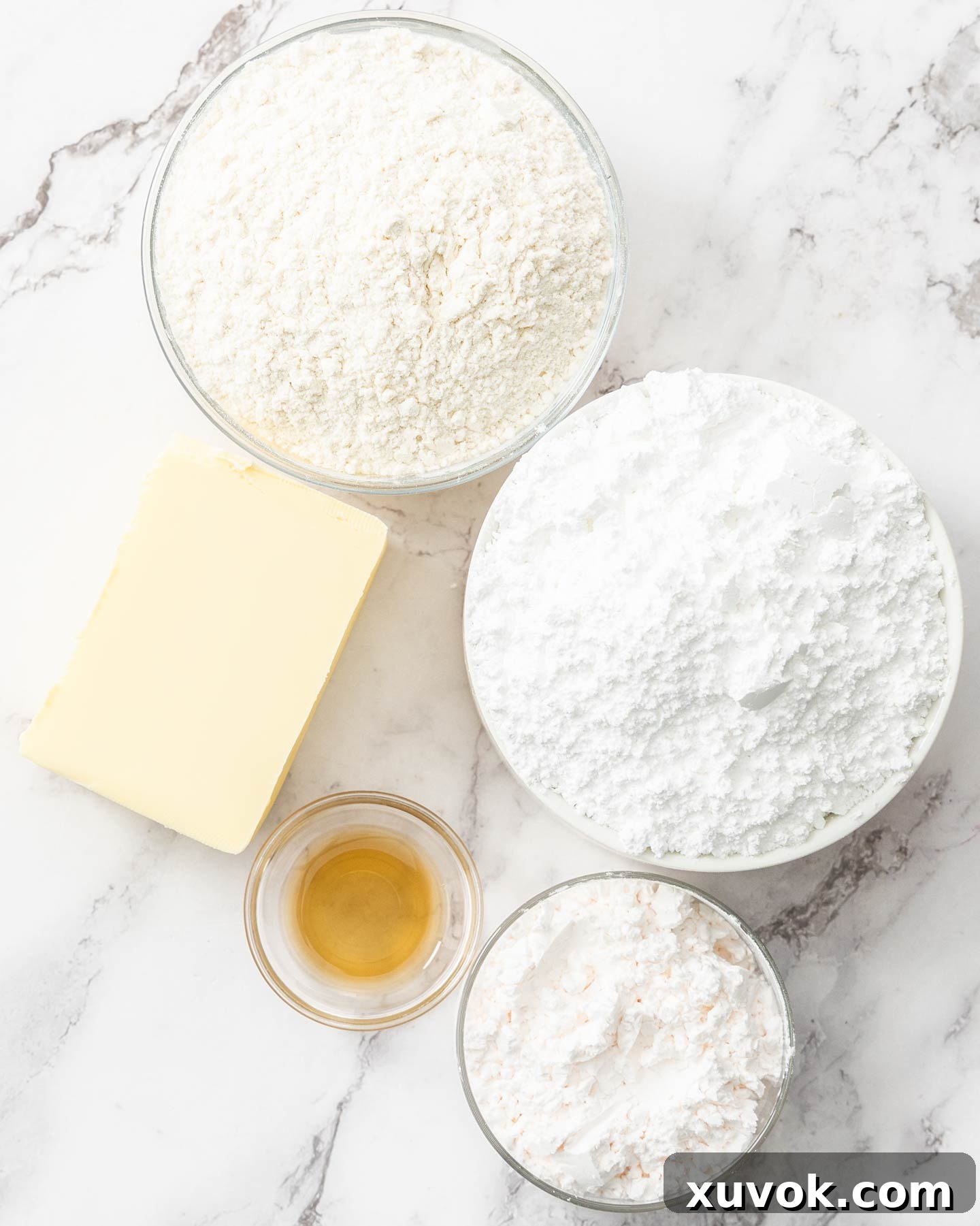 Ingredients for yo yo biscuits laid out on a marble surface, including butter, flour, custard powder, and icing sugar.