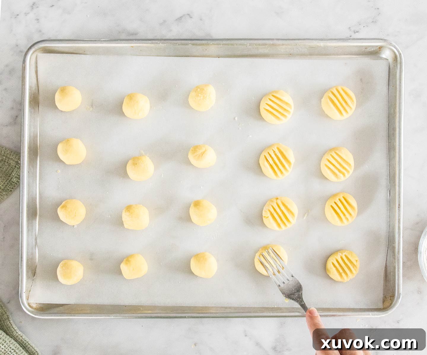 20 balls of cookie dough on a baking tray, some with fork impressions.