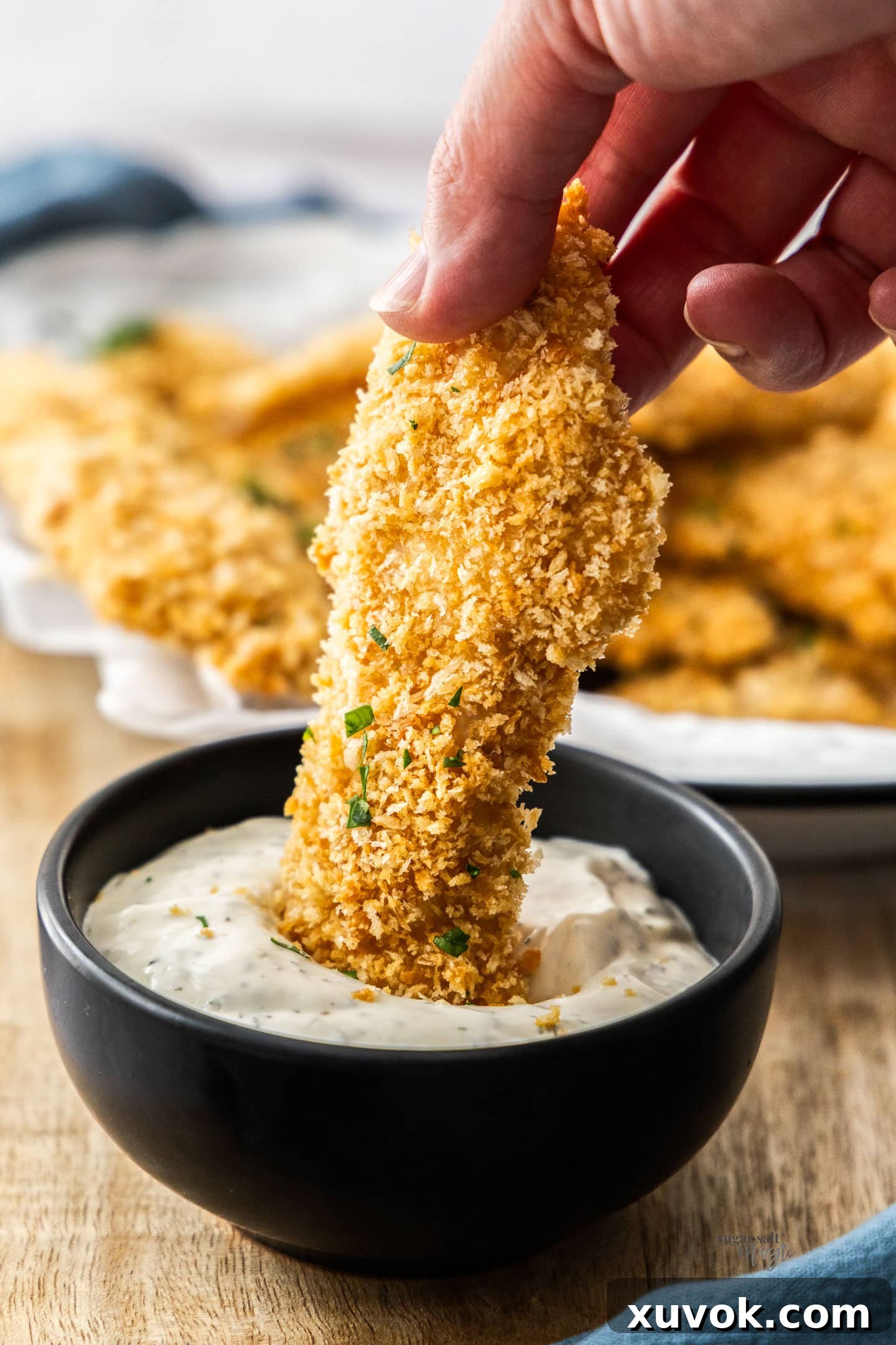 A hand holding a chicken tender dunking into a dip.