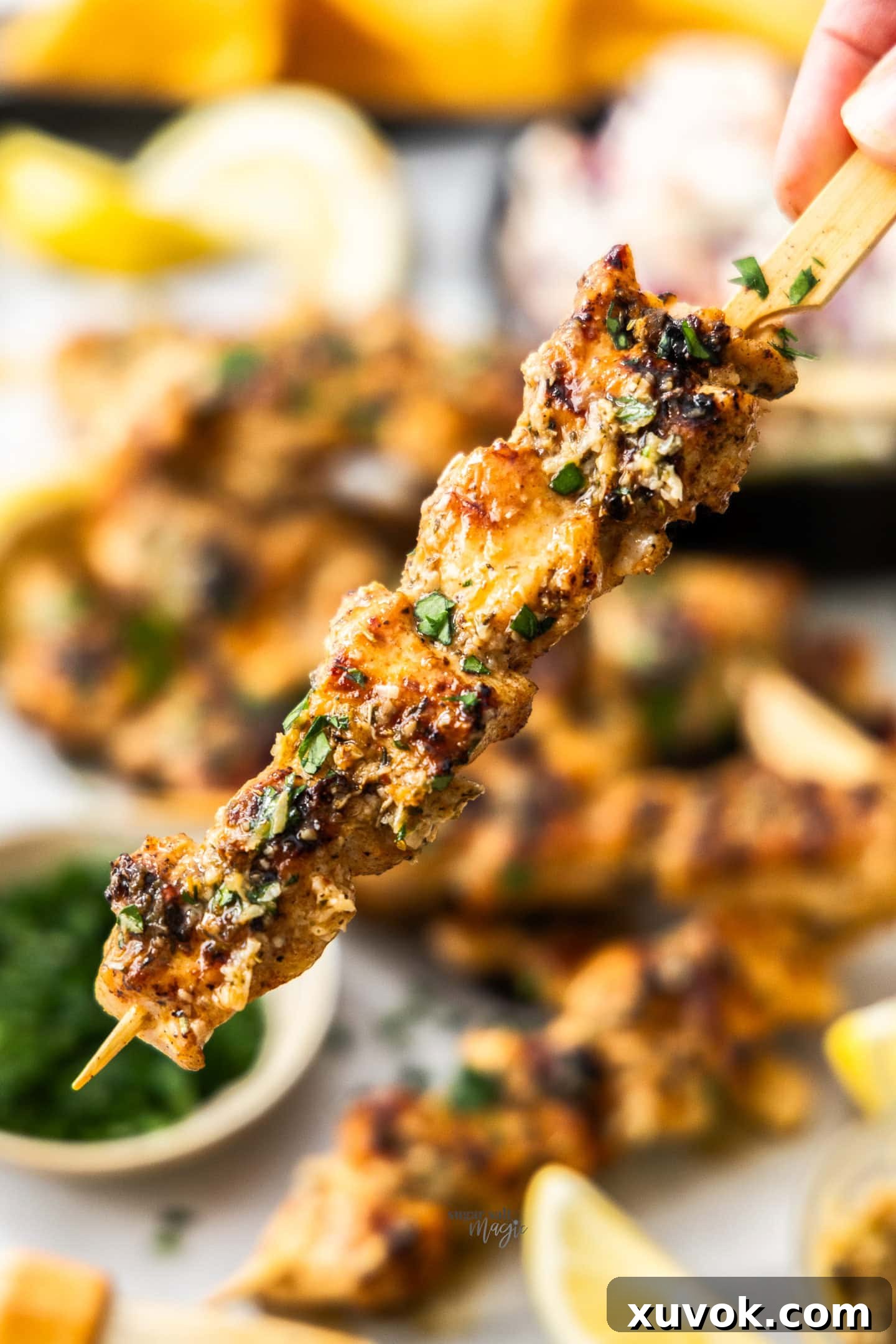A hand holding a perfectly grilled garlic parmesan chicken skewer, showing its golden-brown texture.